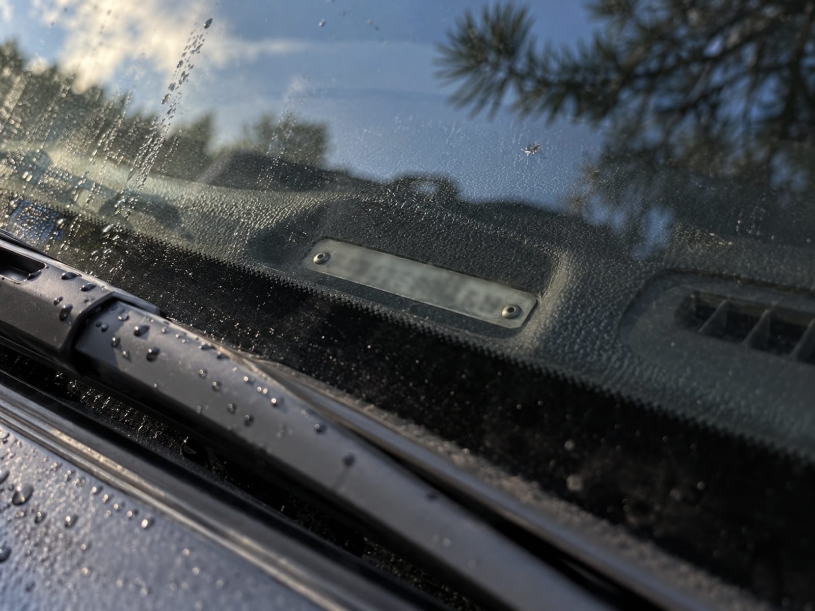 Close view of a vehicle identification number plate at the base of a windshield, digits blurred