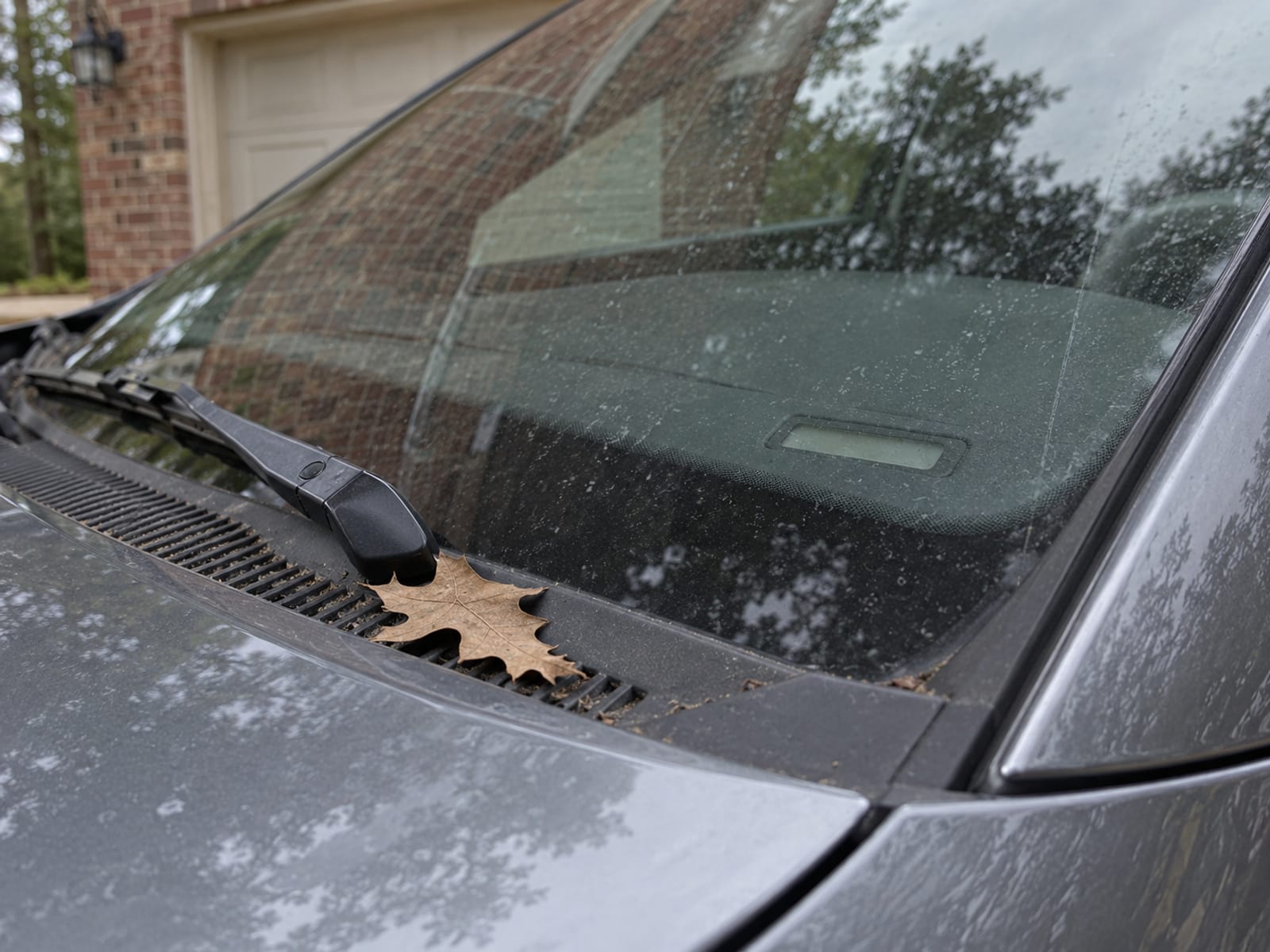 The lower corner of a car windshield in a driveway with the dashboard VIN plate in soft focus