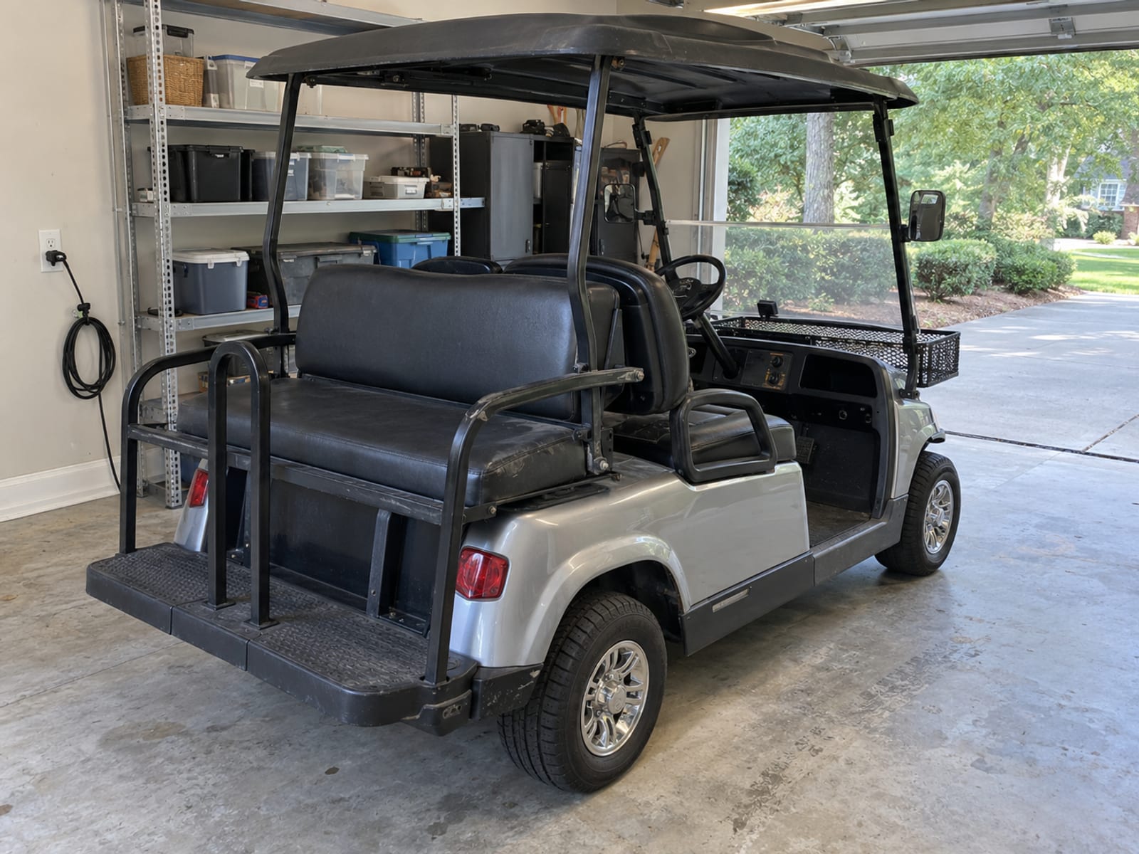 Un carrito de golf con un kit de asiento trasero y una canasta de almacenamiento estacionado en un garaje limpio
