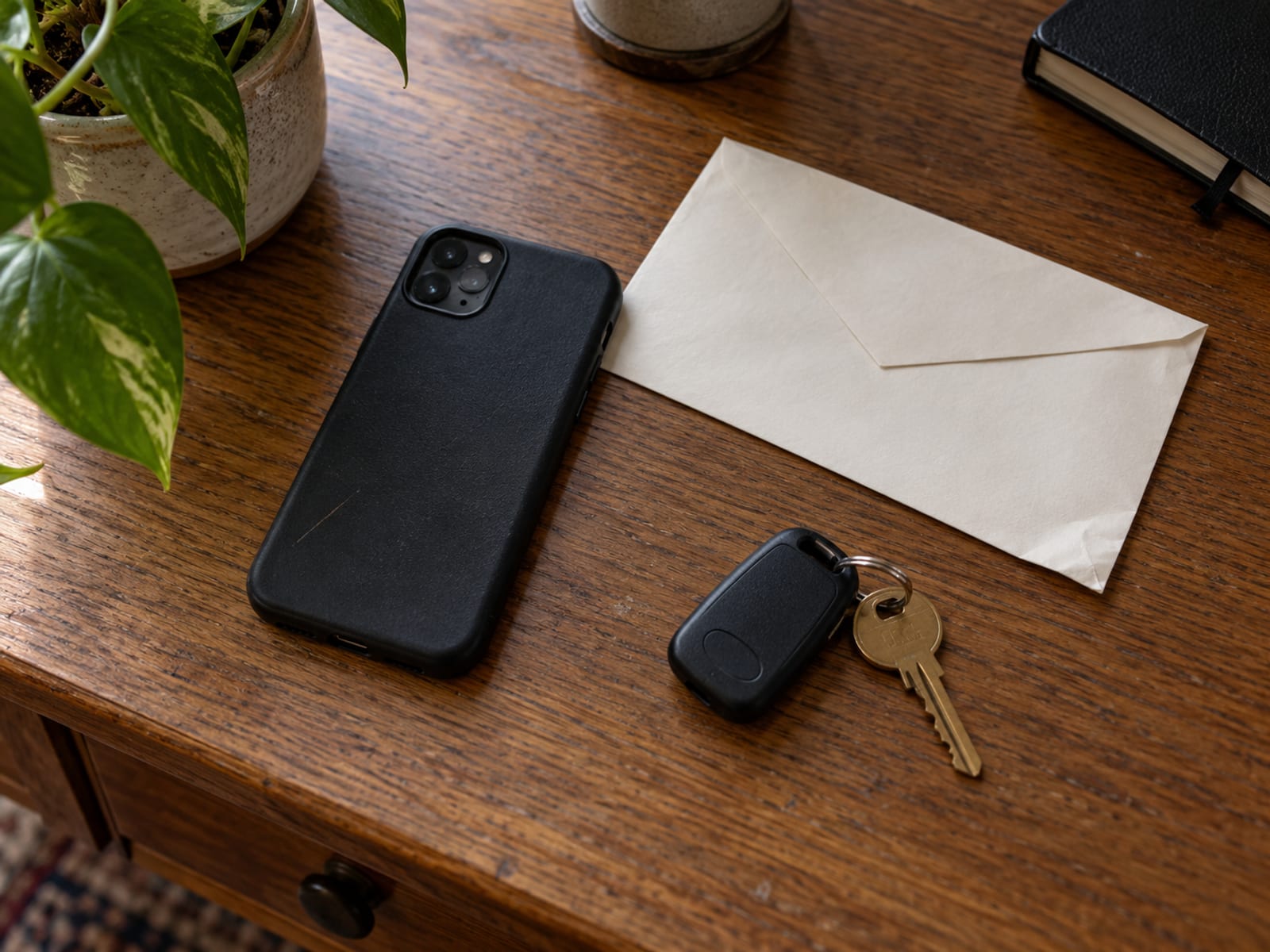 A phone lying face down beside an envelope and car keys on a desk