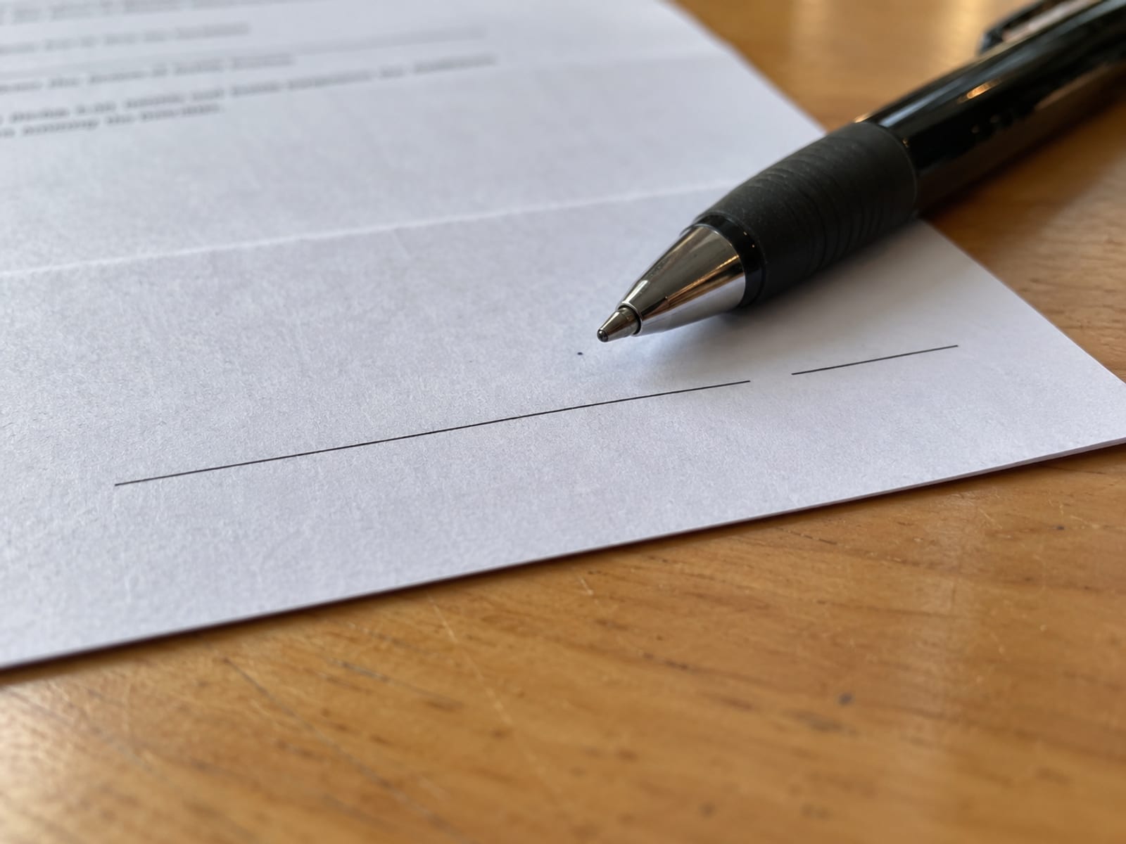 Una pluma apoyada sobre una línea de firma en blanco de un formulario de papel sin marcas en un escritorio