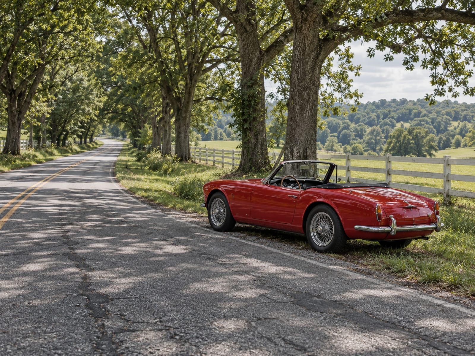 A vintage roadster with no visible plate or badges on an empty country road lined with trees