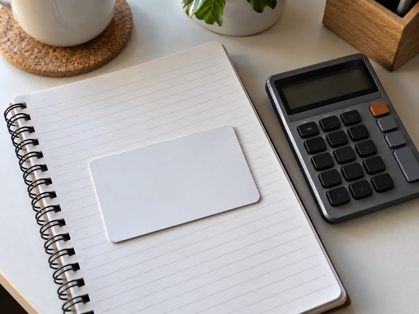 A person's hands holding a blank card above a notepad and a calculator