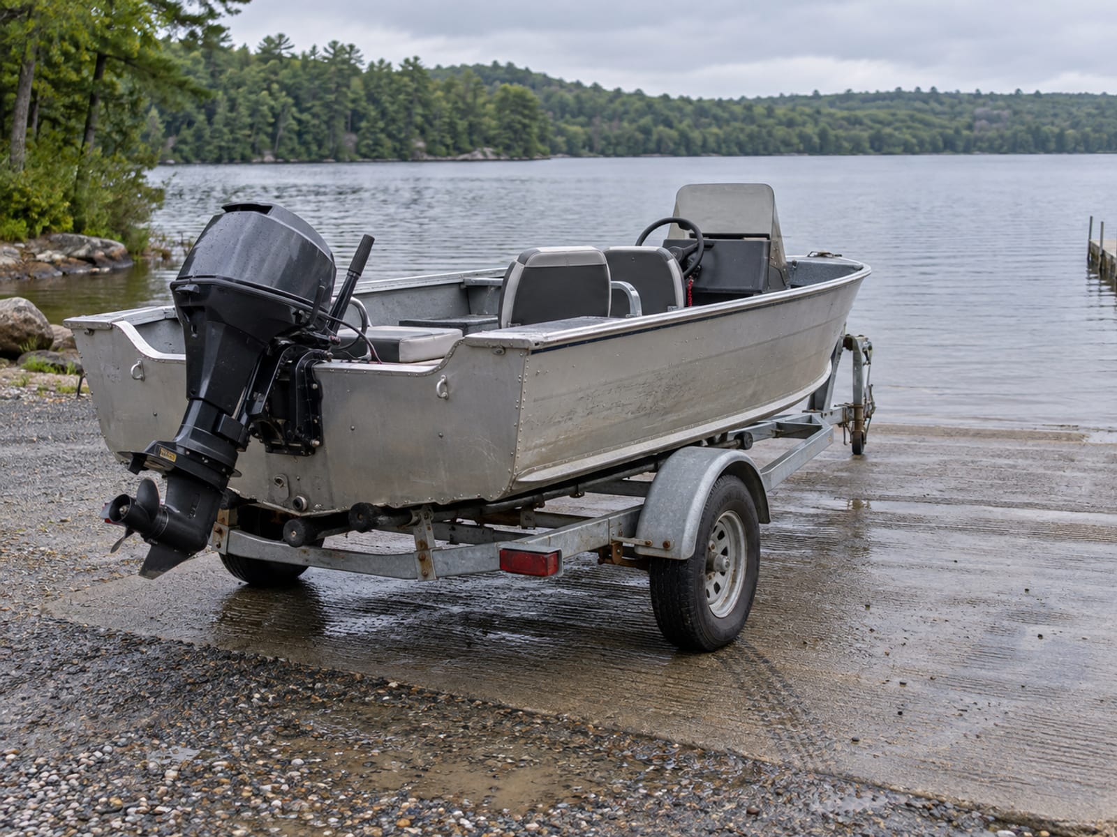 A small motorboat on a trailer at a quiet lakeside boat launch in early morning light