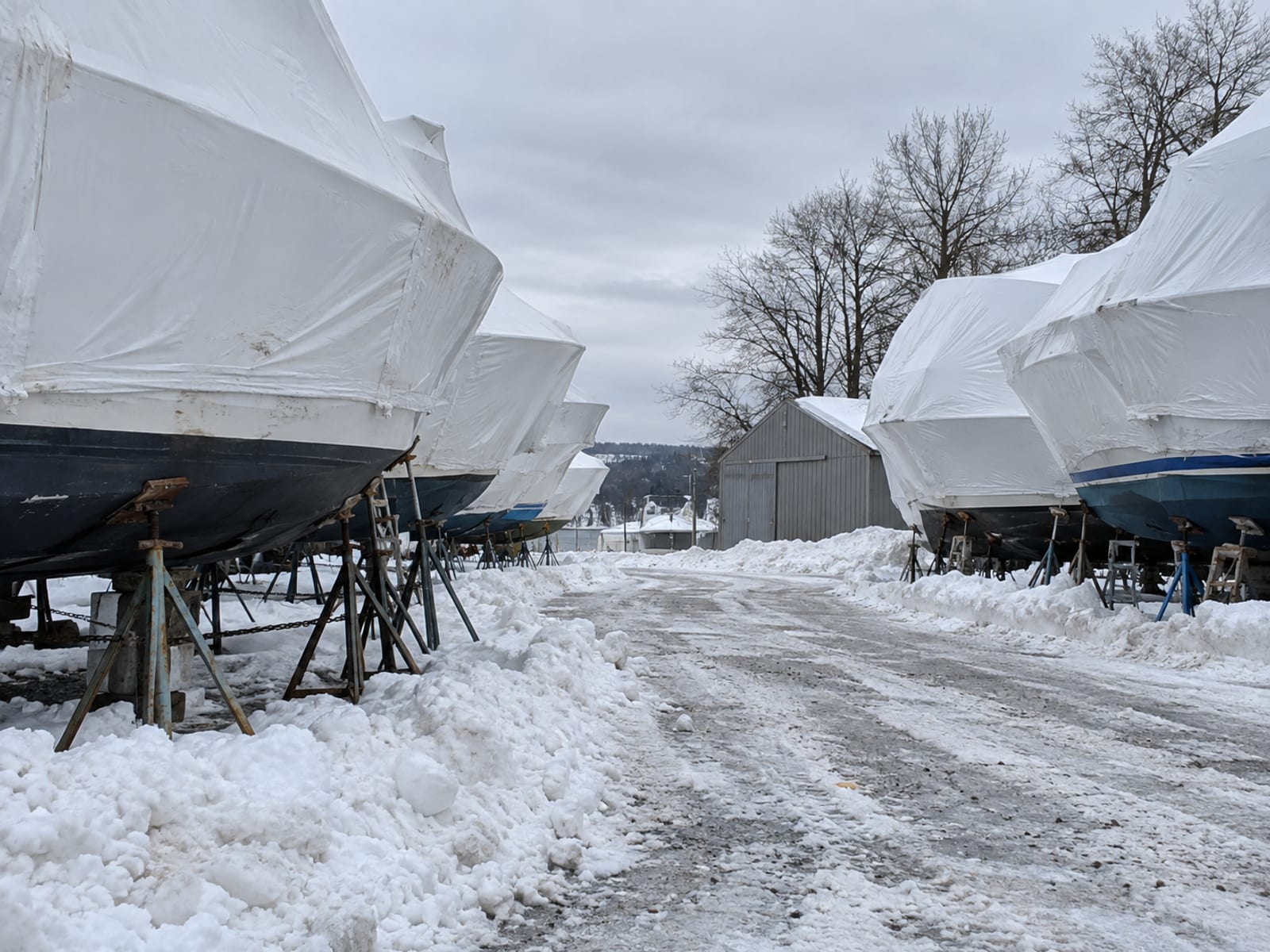 Shrink-wrapped boats on stands in a boatyard with snow on the ground