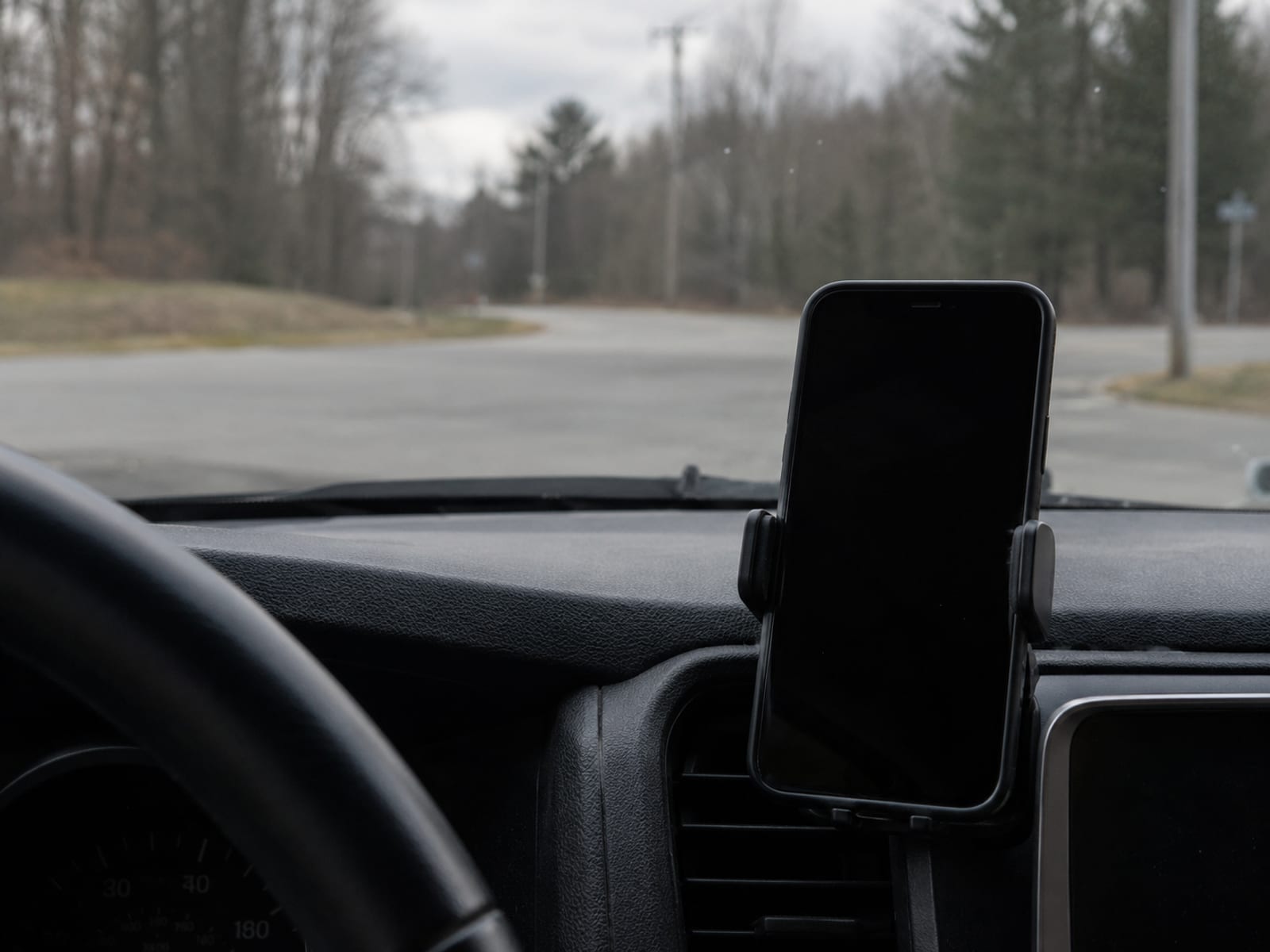 A phone in a dashboard mount with a blank screen inside a car stopped at a rural intersection
