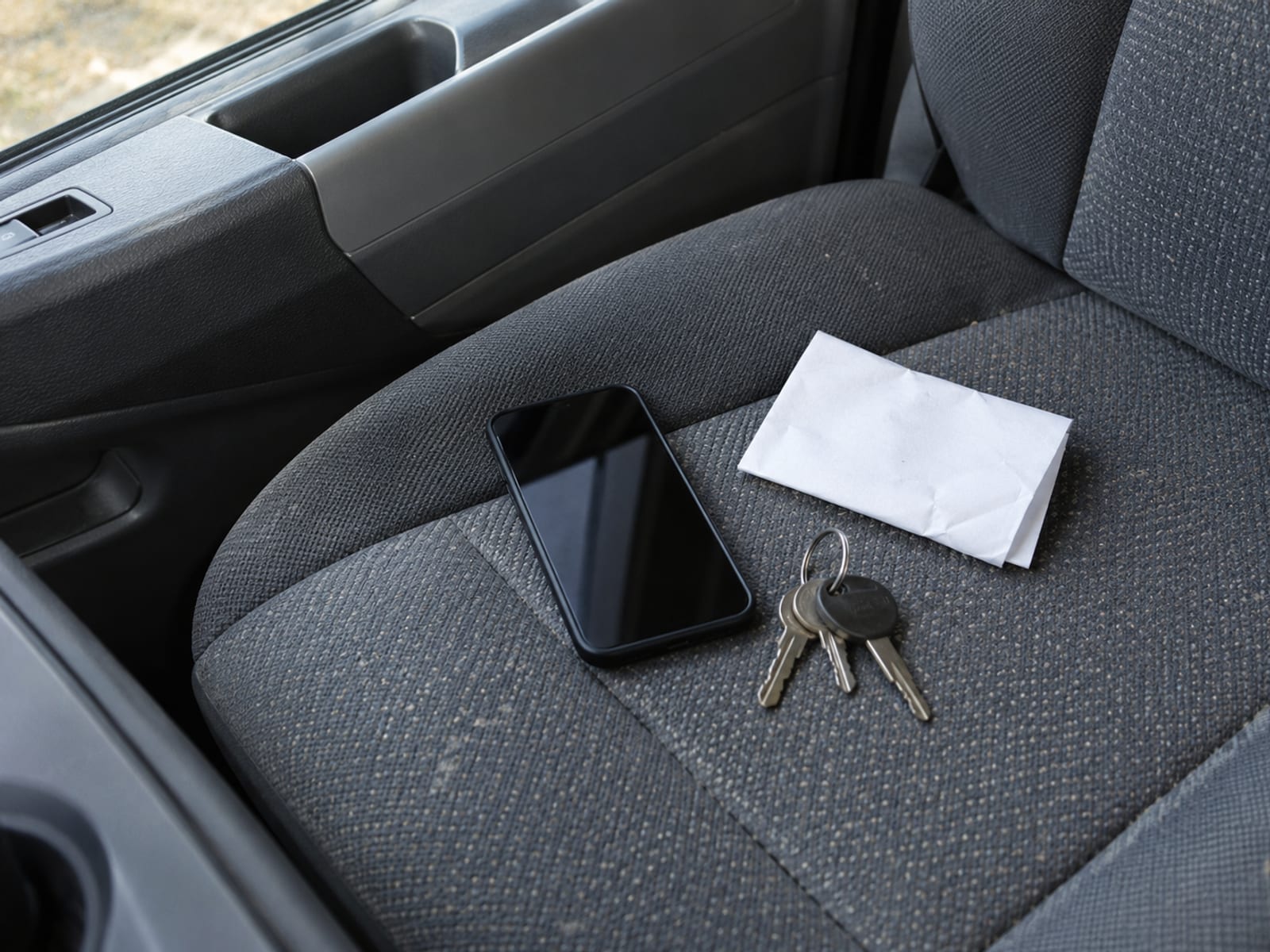 A smartphone with a blank screen next to car keys and a folded document on a car seat