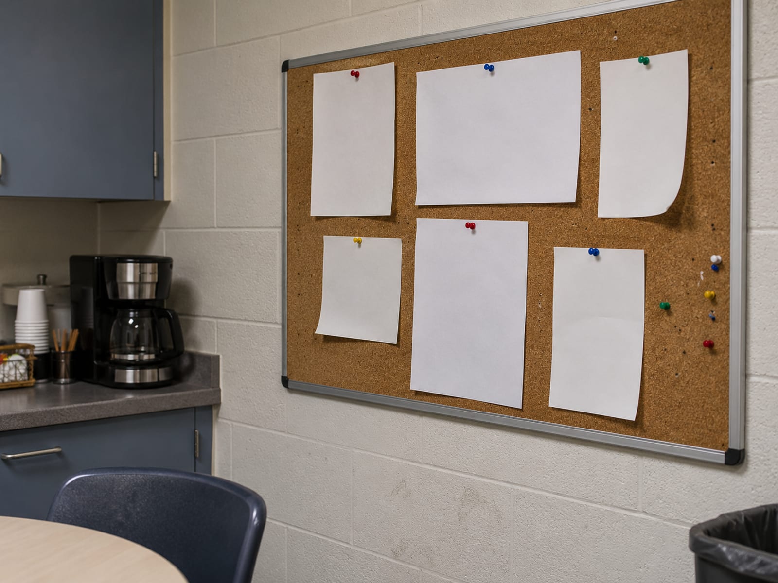A cork bulletin board in an office break room with blank notices pinned to it
