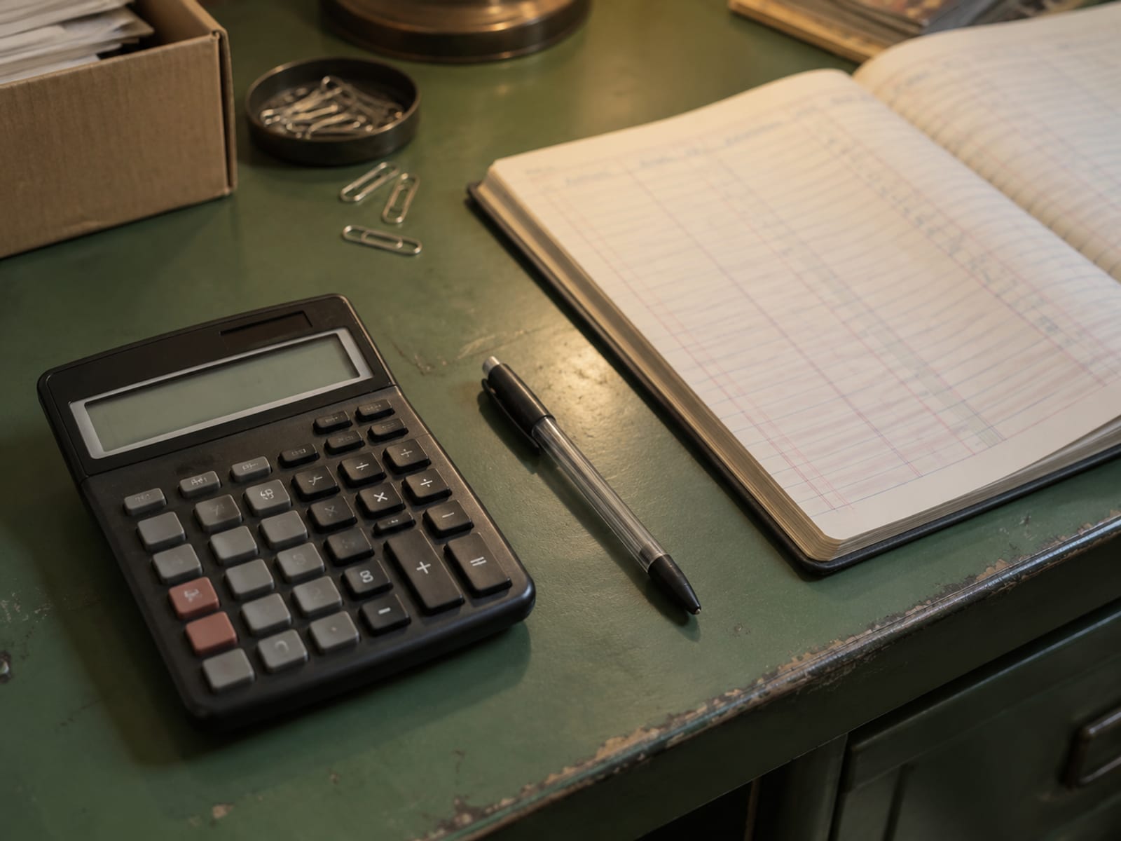 A calculator, a pen and a printed payroll ledger with blurred figures on a wooden desk