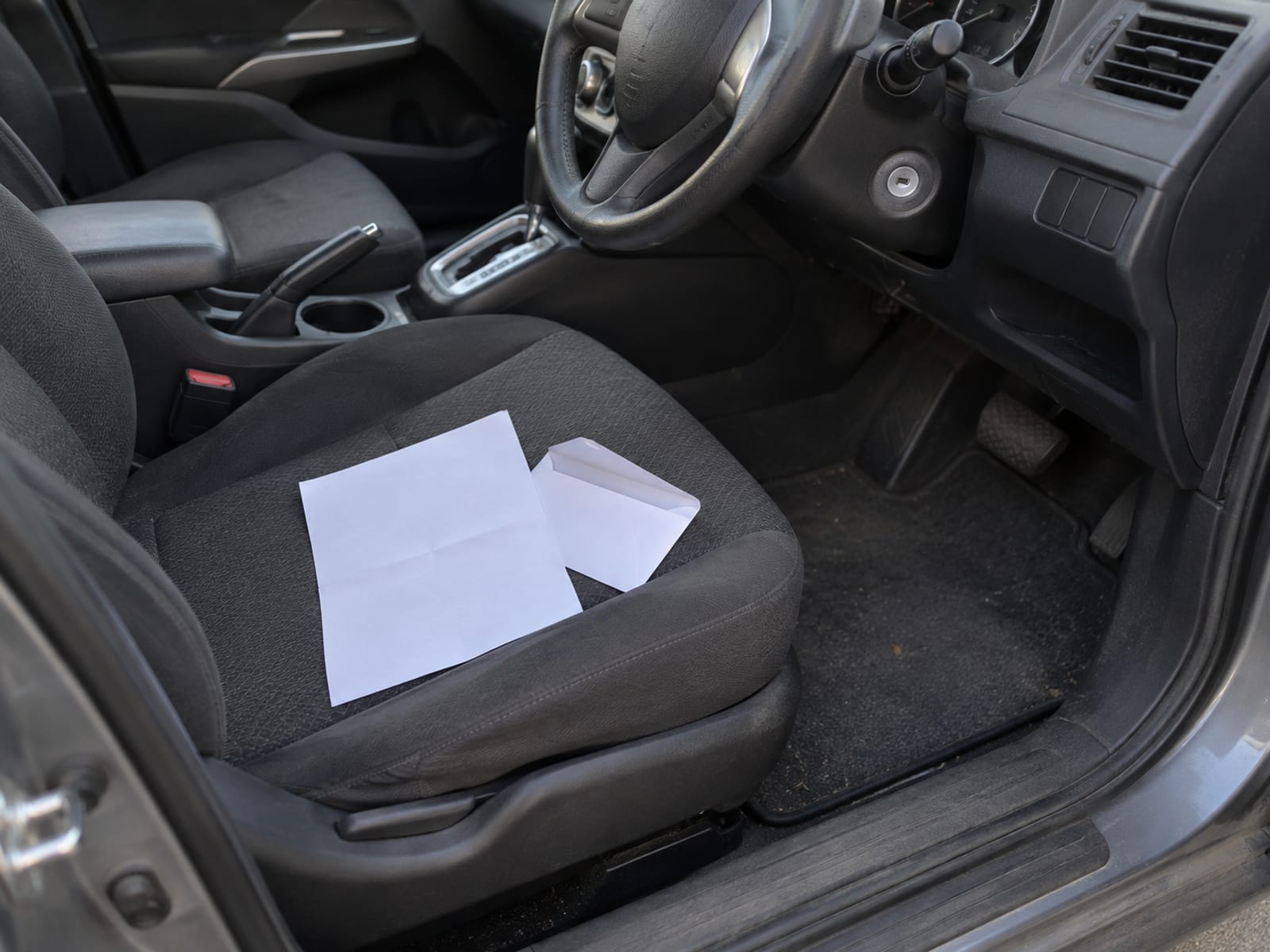 A plain blank letter and an envelope resting on the driver seat of a parked car in daylight