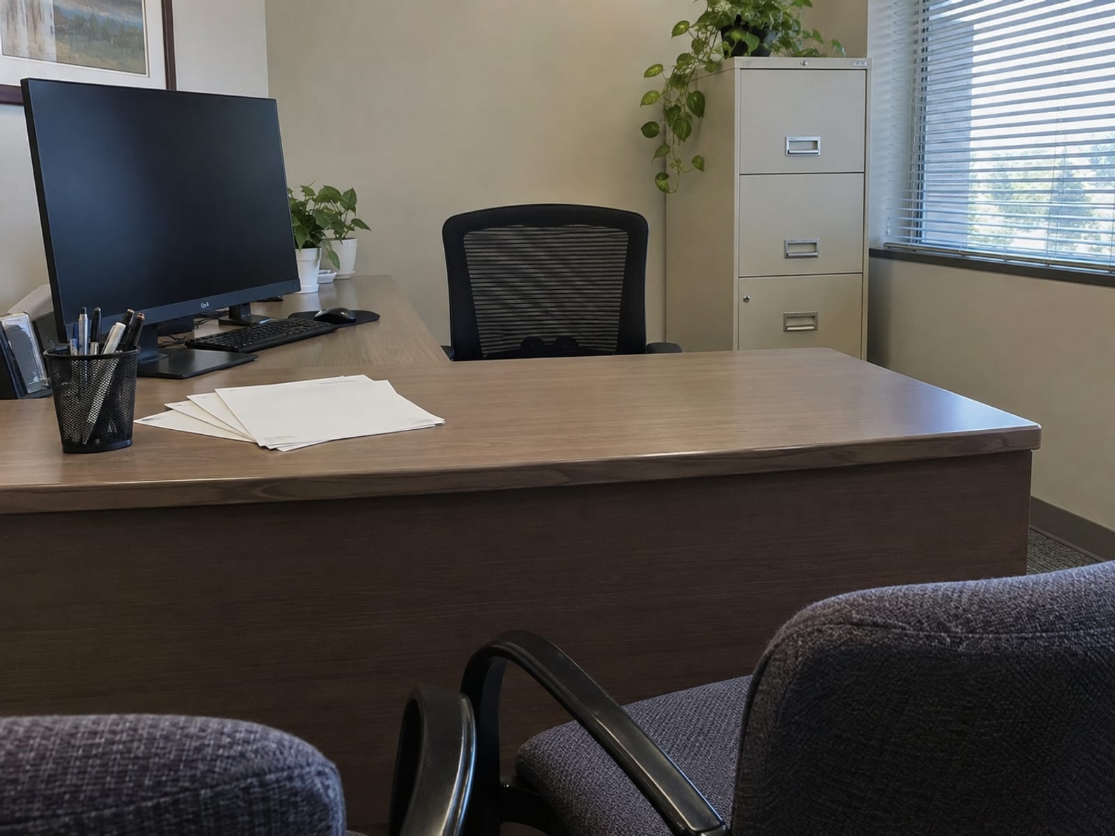 Two chairs pulled up to an office desk covered with blank forms and a pen cup