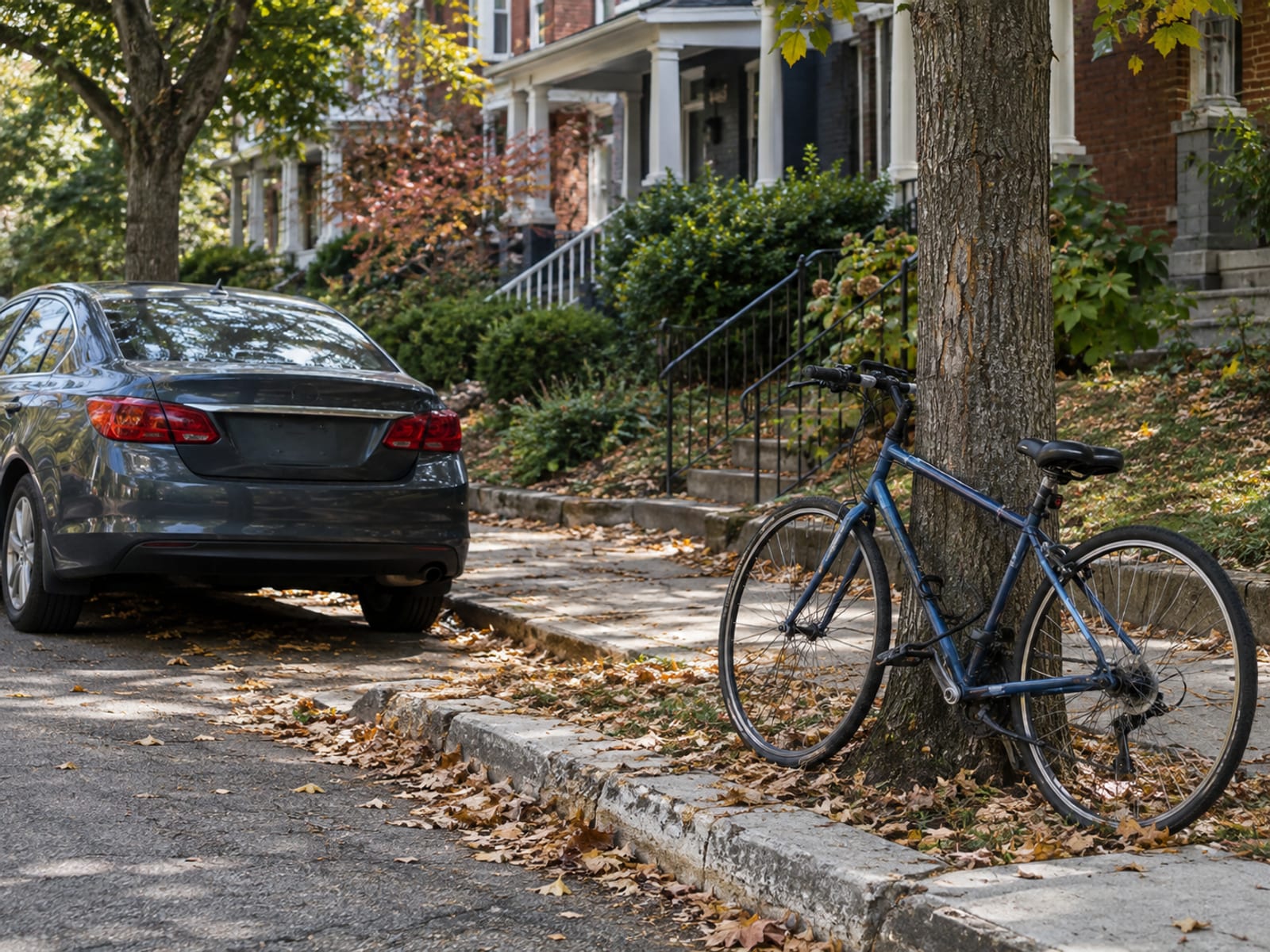 A parked car at the curb on a quiet residential street with a bicycle leaning against a tree nearby