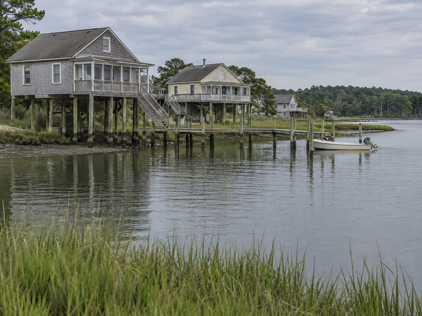 Waterfront homes raised on pilings along a quiet Chesapeake Bay inlet under a cloudy sky
