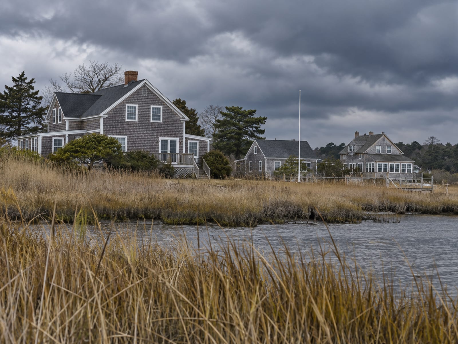 Shingled waterfront homes on the Eastern Shore under gathering clouds with marsh grass in front