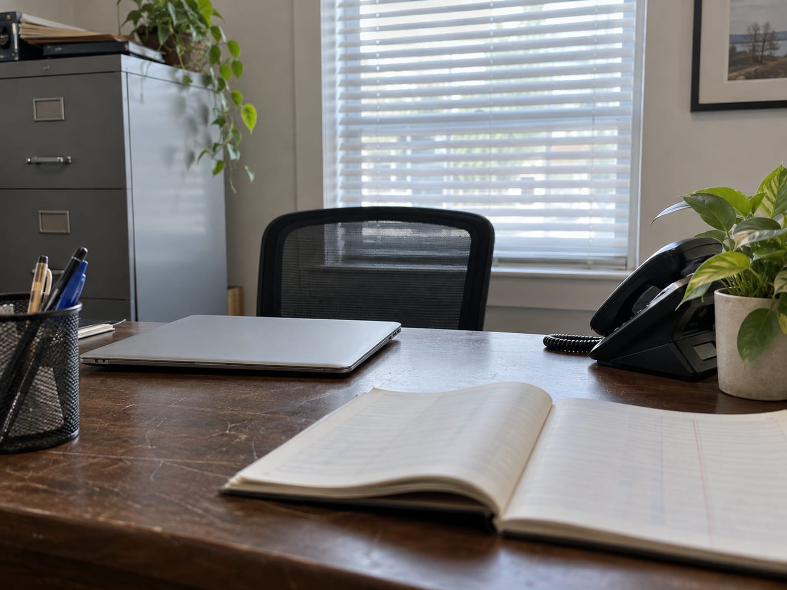 A small business office desk with a laptop, a printed payroll ledger with blurred lines, and a coffee mug