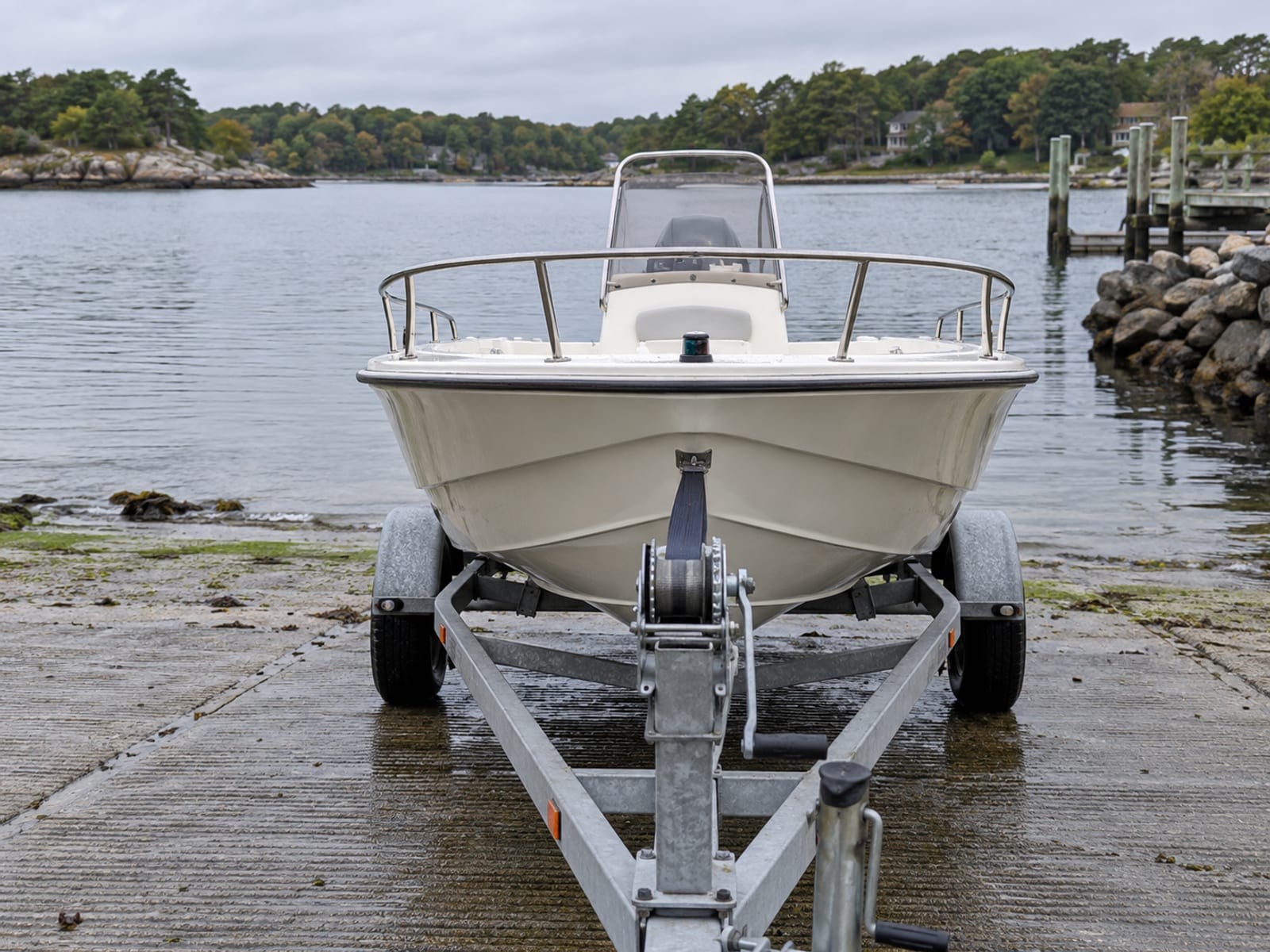 The bow of a small outboard motorboat on a trailer at a boat ramp with a lake in the background
