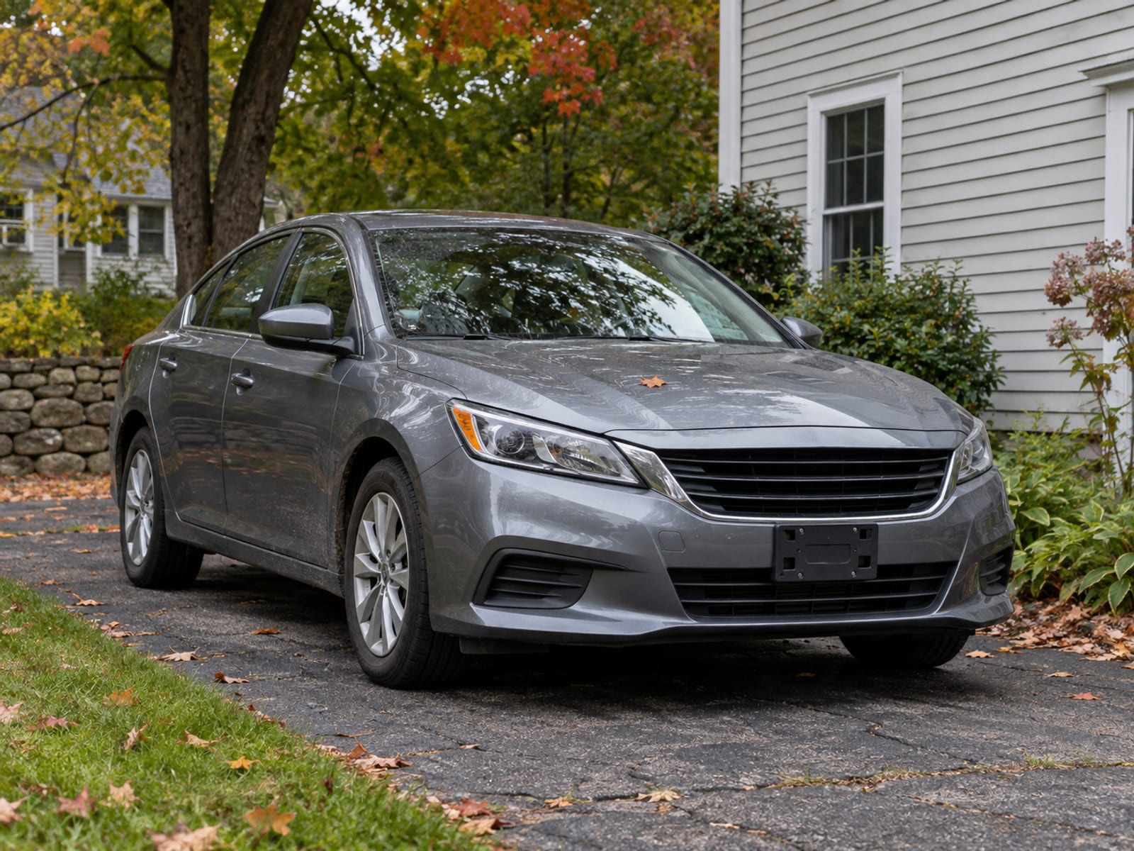 A sedan without a front license plate parked in a residential driveway beside maple trees