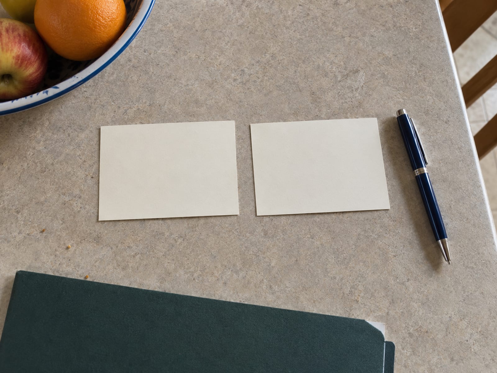 Two blank plastic insurance cards beside a pen and a closed folder on a kitchen table