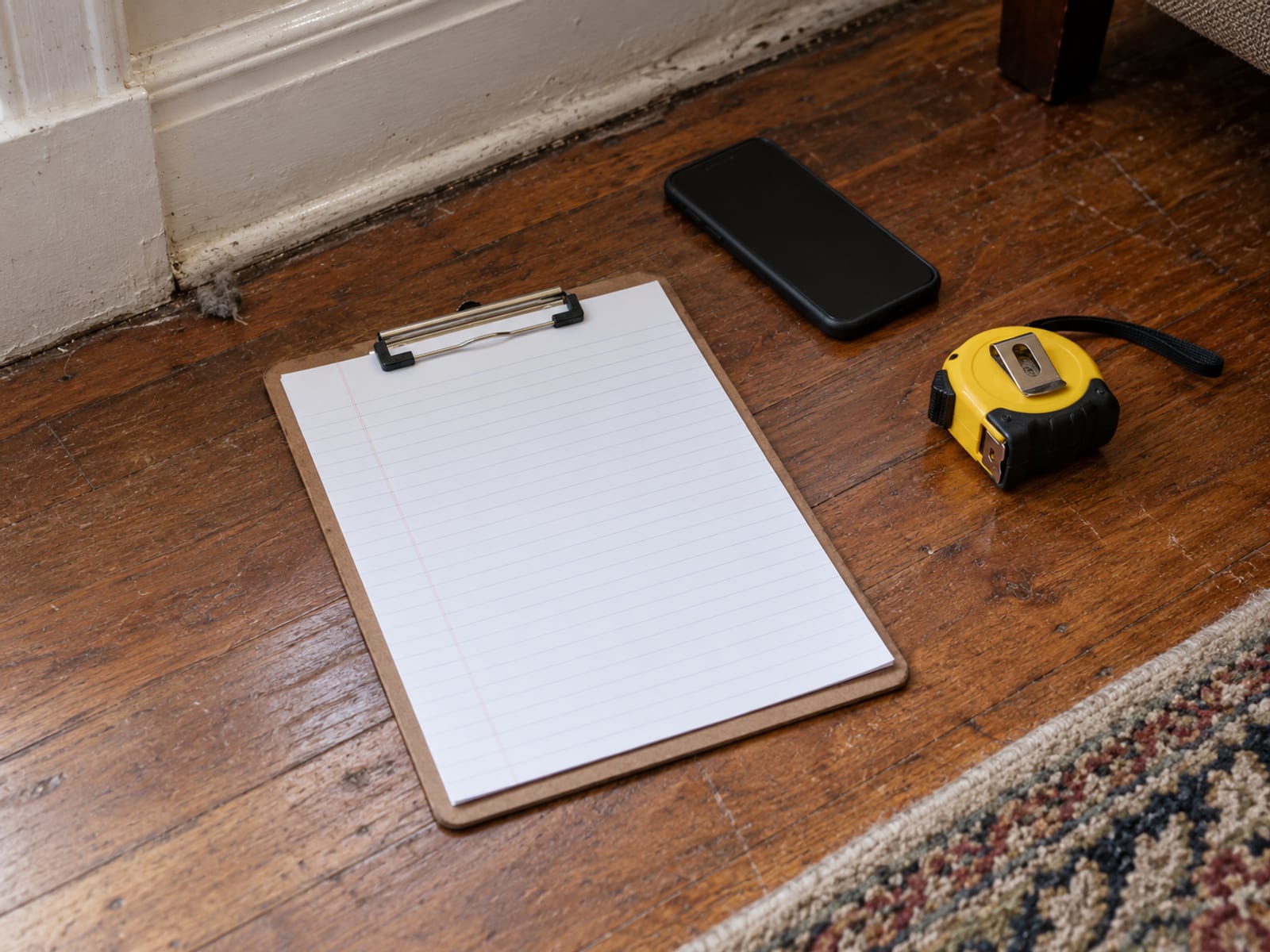 A clipboard with a blank inventory sheet, a phone and a tape measure on a wooden floor
