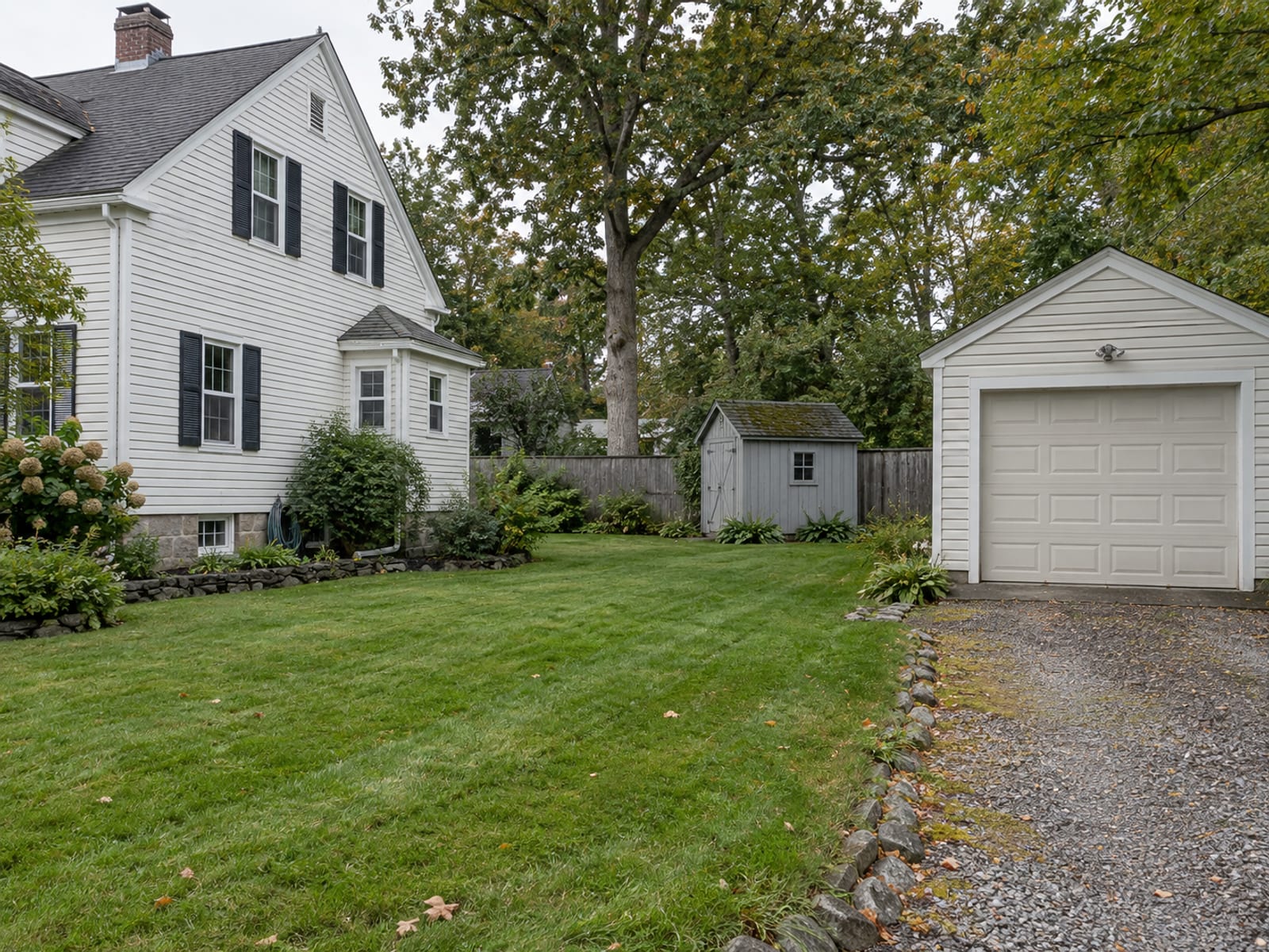 A New England colonial house with a detached garage and a small shed in the yard