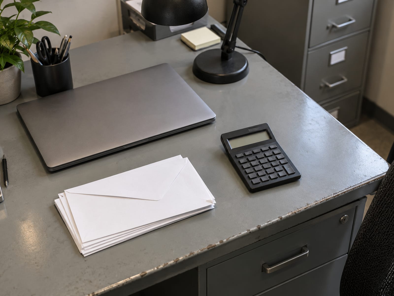 A desk with a closed laptop, a calculator and a stack of blank envelopes