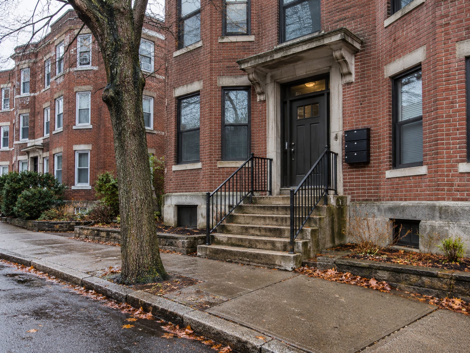 The front steps and entrance of a three-story brick apartment building on a quiet street