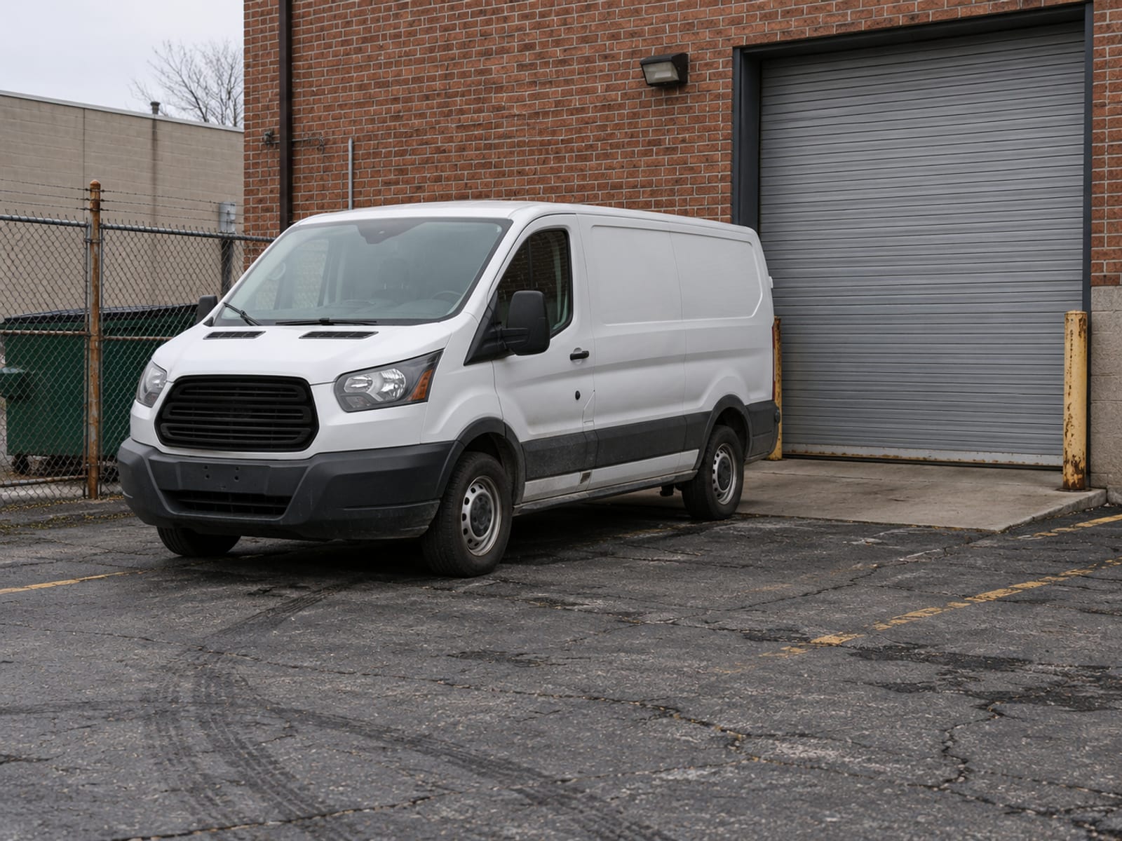 An unmarked white work van parked in a small business lot beside a loading door