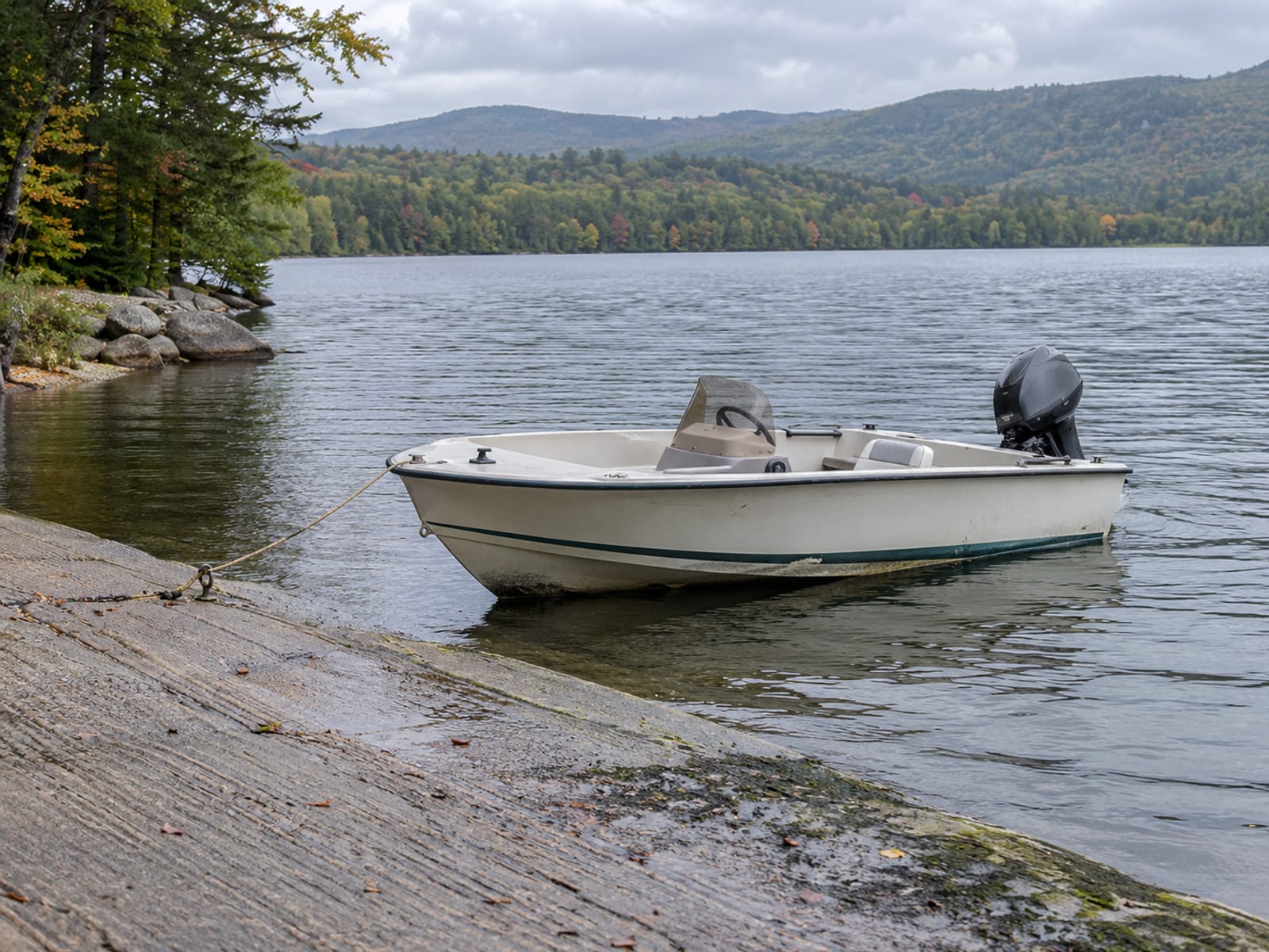 An empty runabout with an outboard motor idling at a public launch ramp on a quiet lake