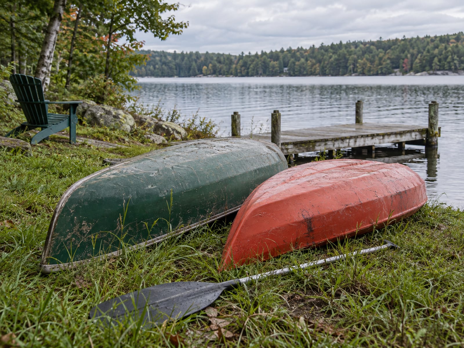 A canoe and a kayak resting upside down on a grassy lakeshore beside a small cottage dock