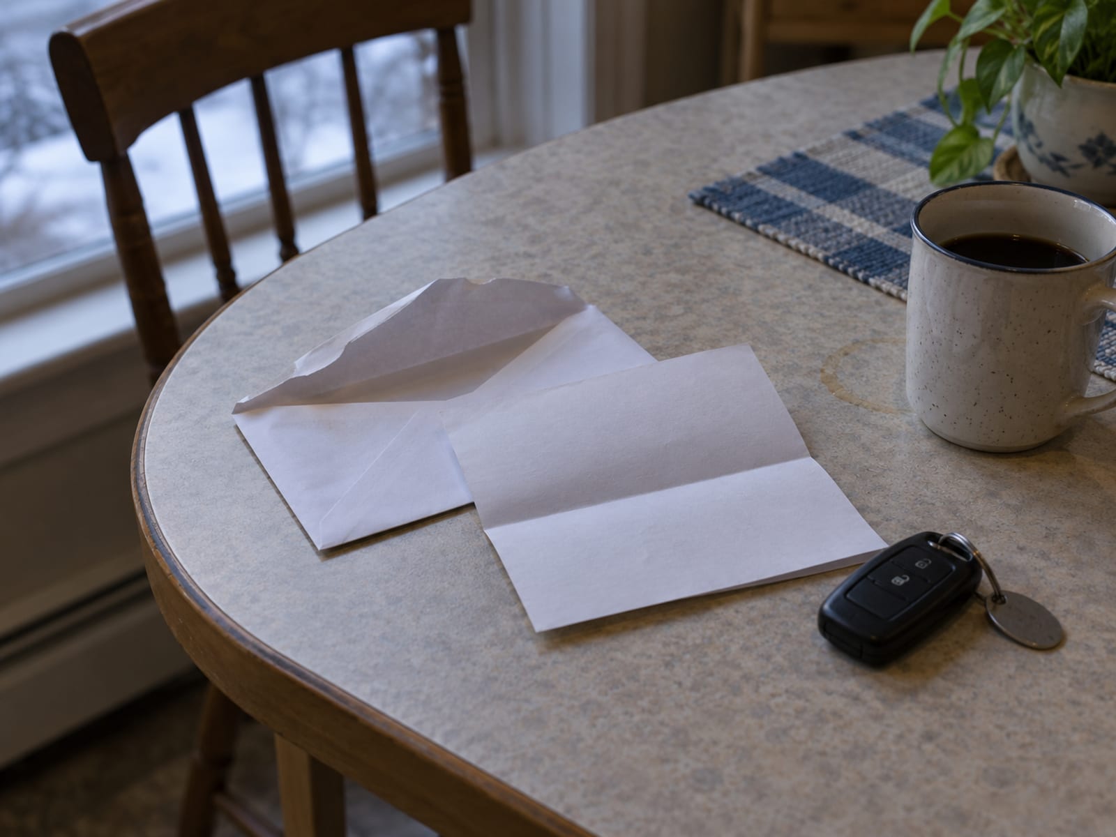 An opened envelope and a folded notice letter beside a car key on a kitchen table, with no readable text