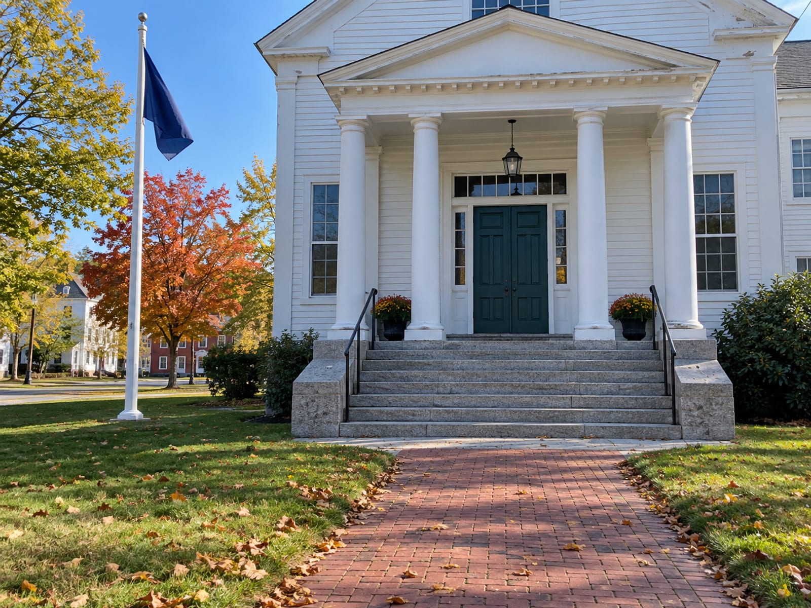 The front steps of a white New England town hall with a flagpole on a clear morning