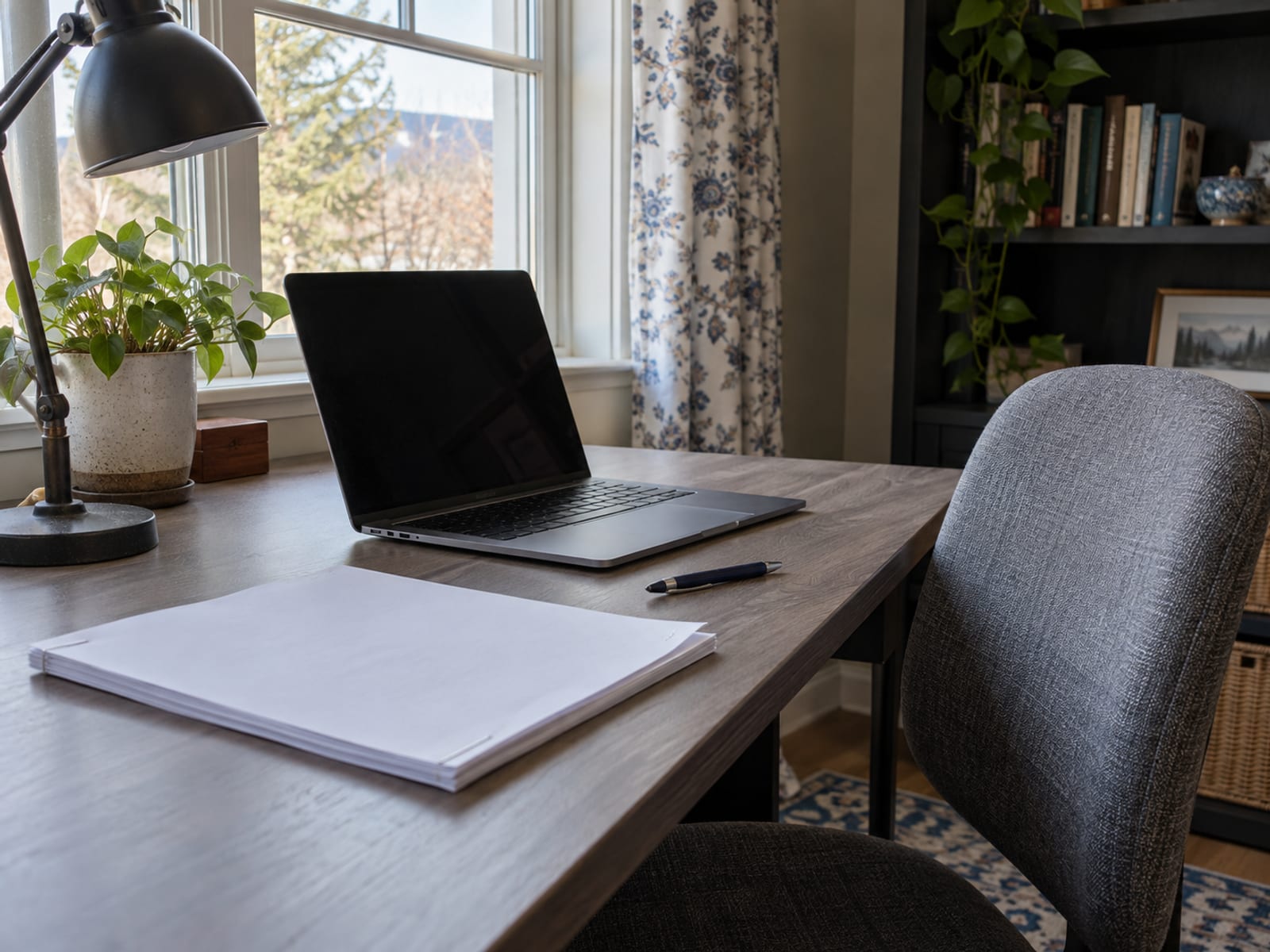 A benefits enrollment packet, a laptop and a cup of tea on a home desk beside an empty chair