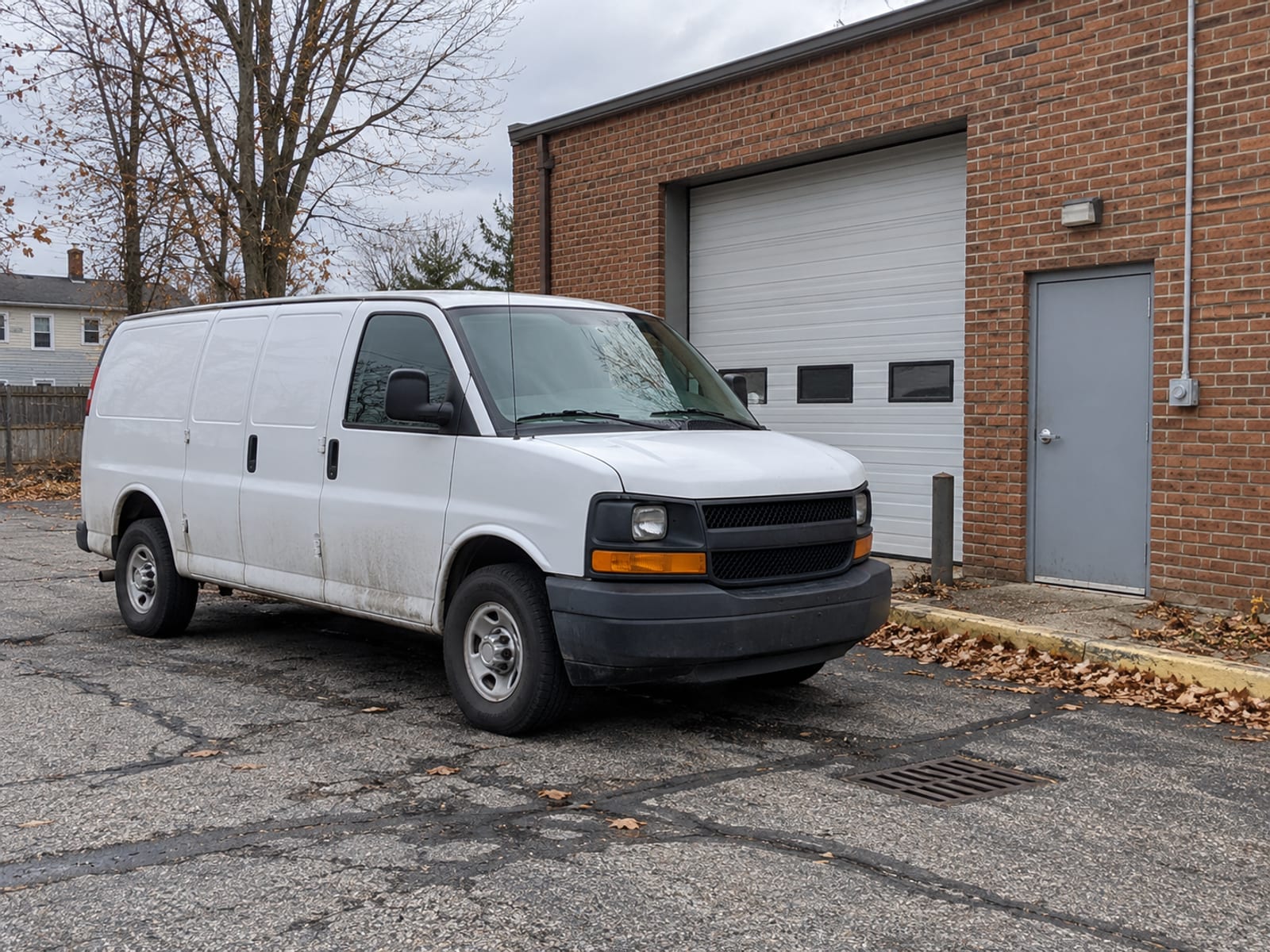 An unmarked white work van parked beside a small brick commercial building on a quiet street