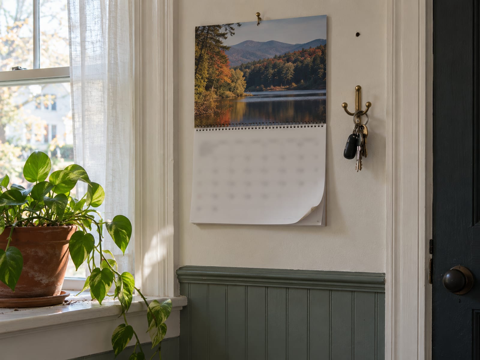 A wall calendar beside a window with a houseplant on the sill and a set of keys on a hook