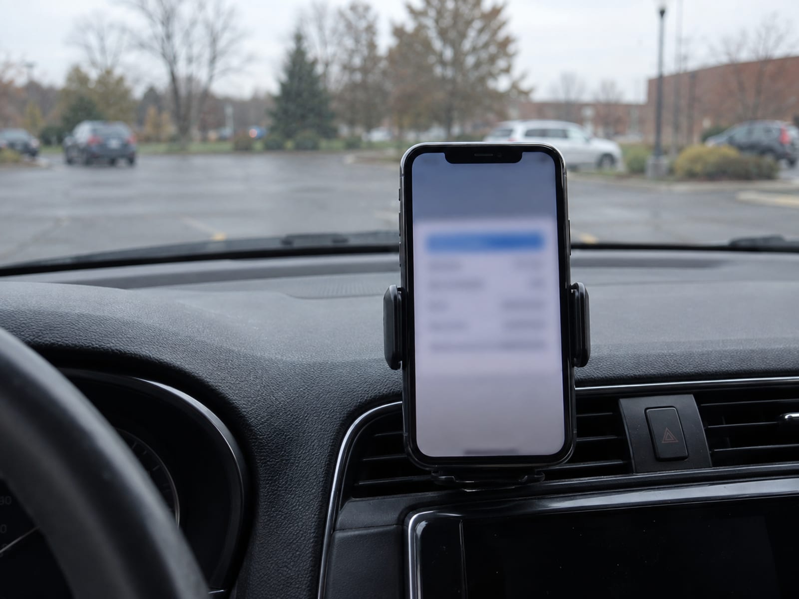 A smartphone in a dashboard mount showing a blurred card image, seen from the driver seat