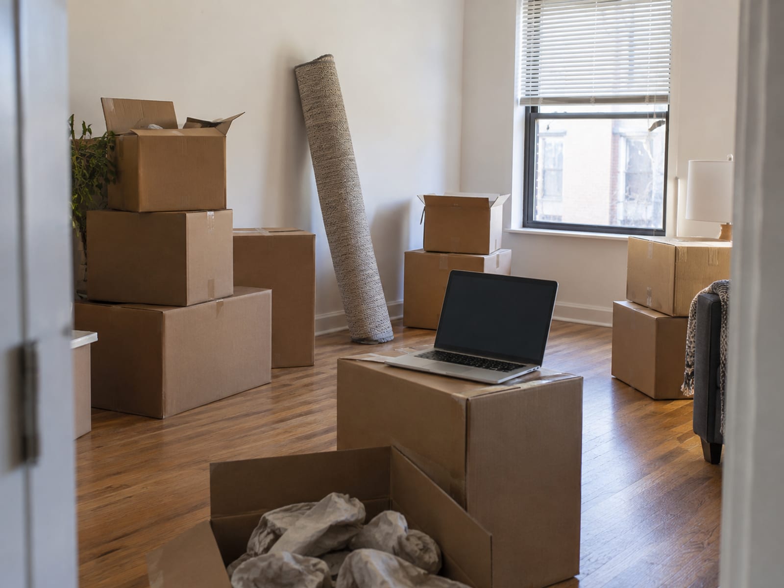 Moving boxes stacked in a bright apartment entryway with a laptop open on one of the boxes