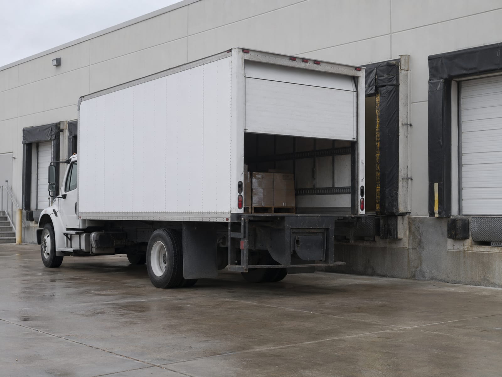 A plain white box truck parked beside a warehouse loading dock on an overcast morning
