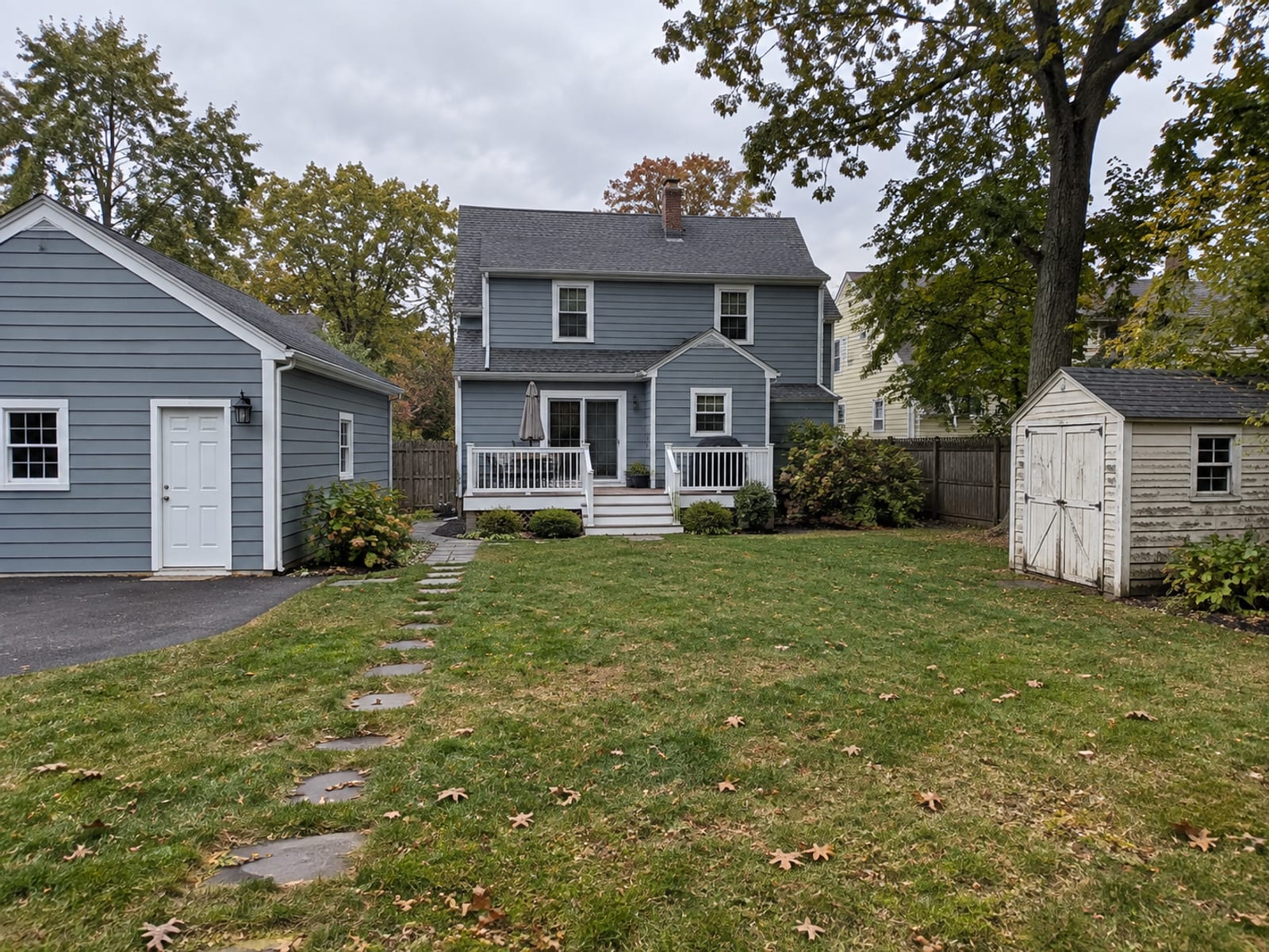 A New York style two-story house with a detached garage and a small shed in a yard