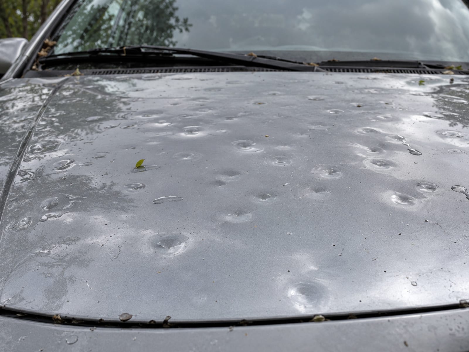 The hood of a parked sedan dented by hail, close up