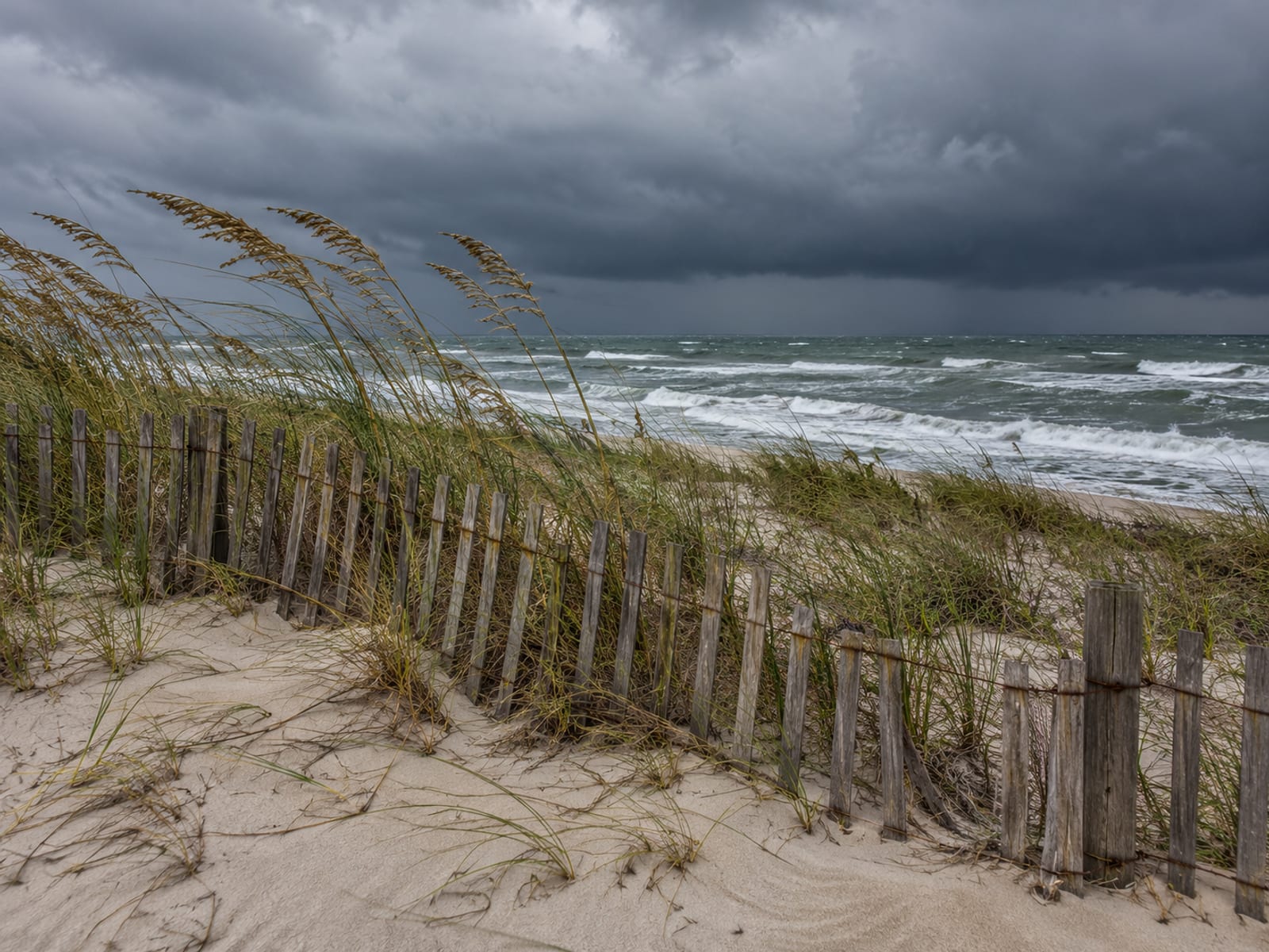 Storm clouds gathering over the ocean behind a dune fence