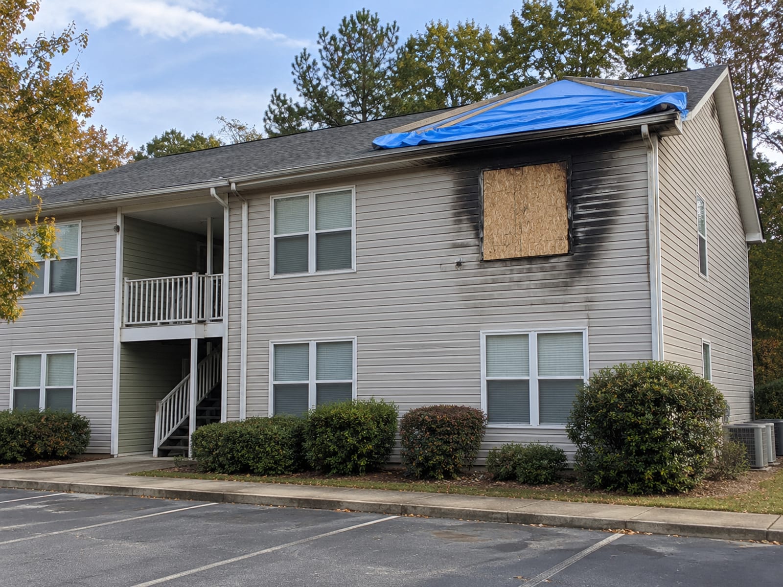 A two-story apartment building with a fire-damaged upper window and a tarp over part of the roof