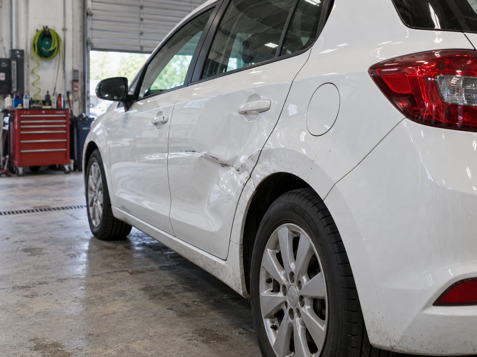 A dented rear door and quarter panel on a parked car in a repair shop bay
