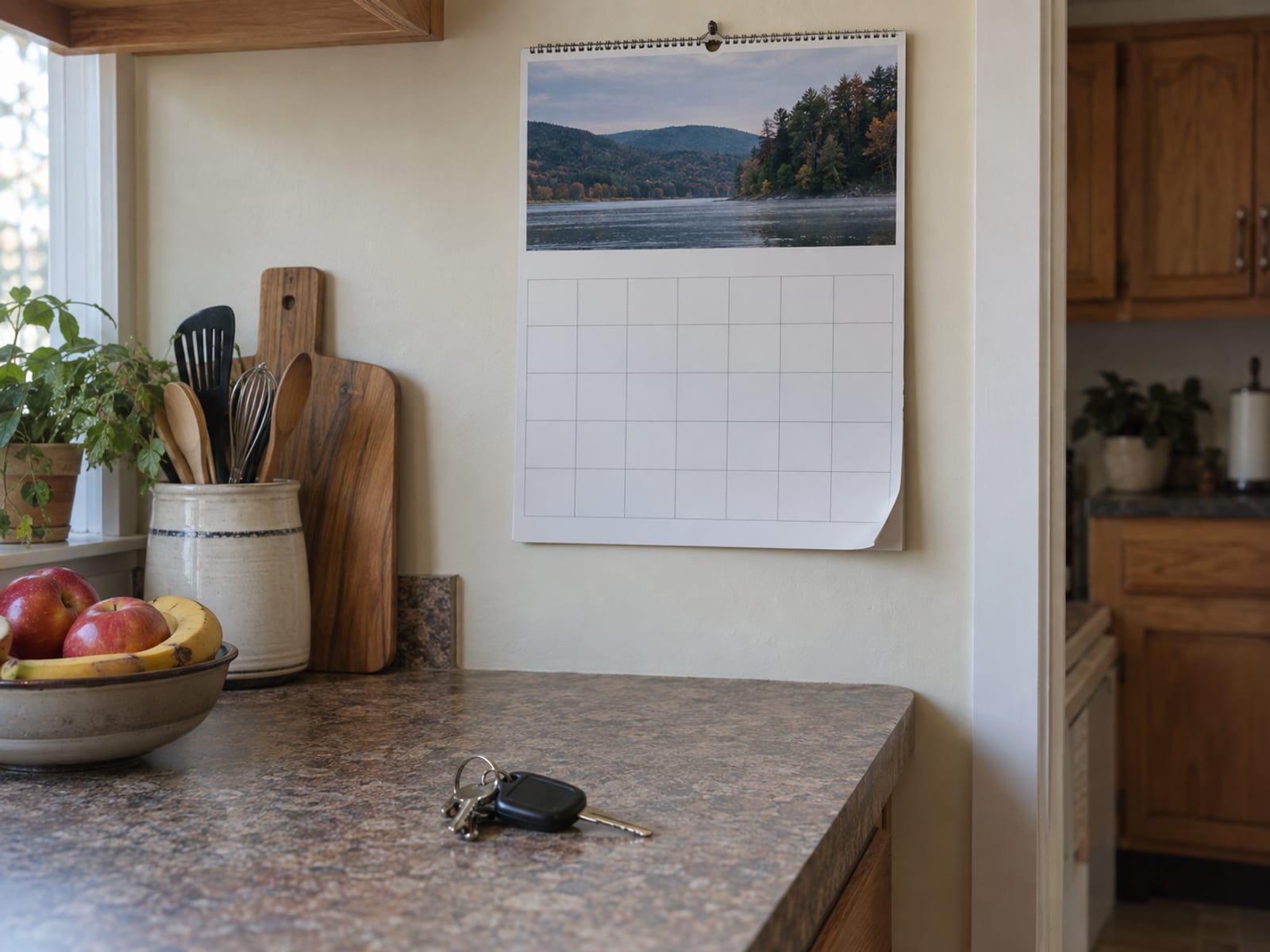 A wall calendar with blank date squares hanging above a kitchen counter beside a set of car keys