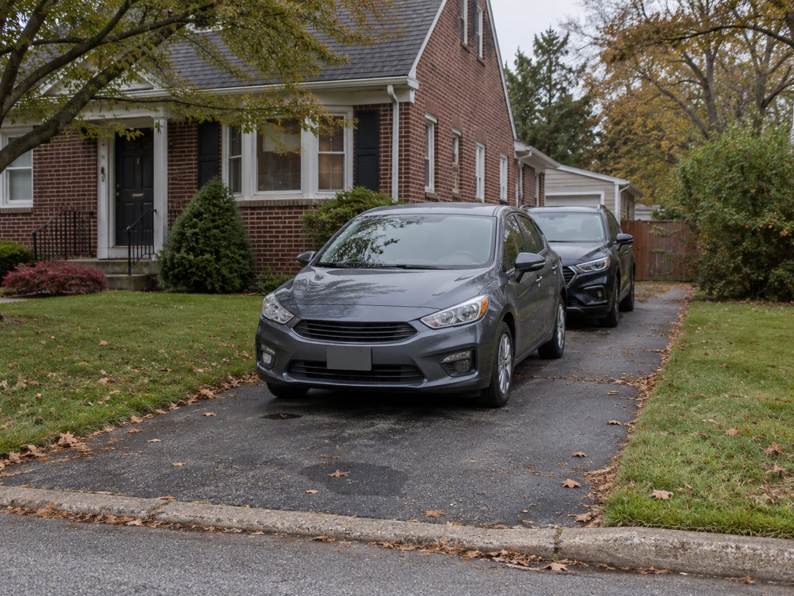 A compact car parked in a suburban driveway with a second car parked behind it