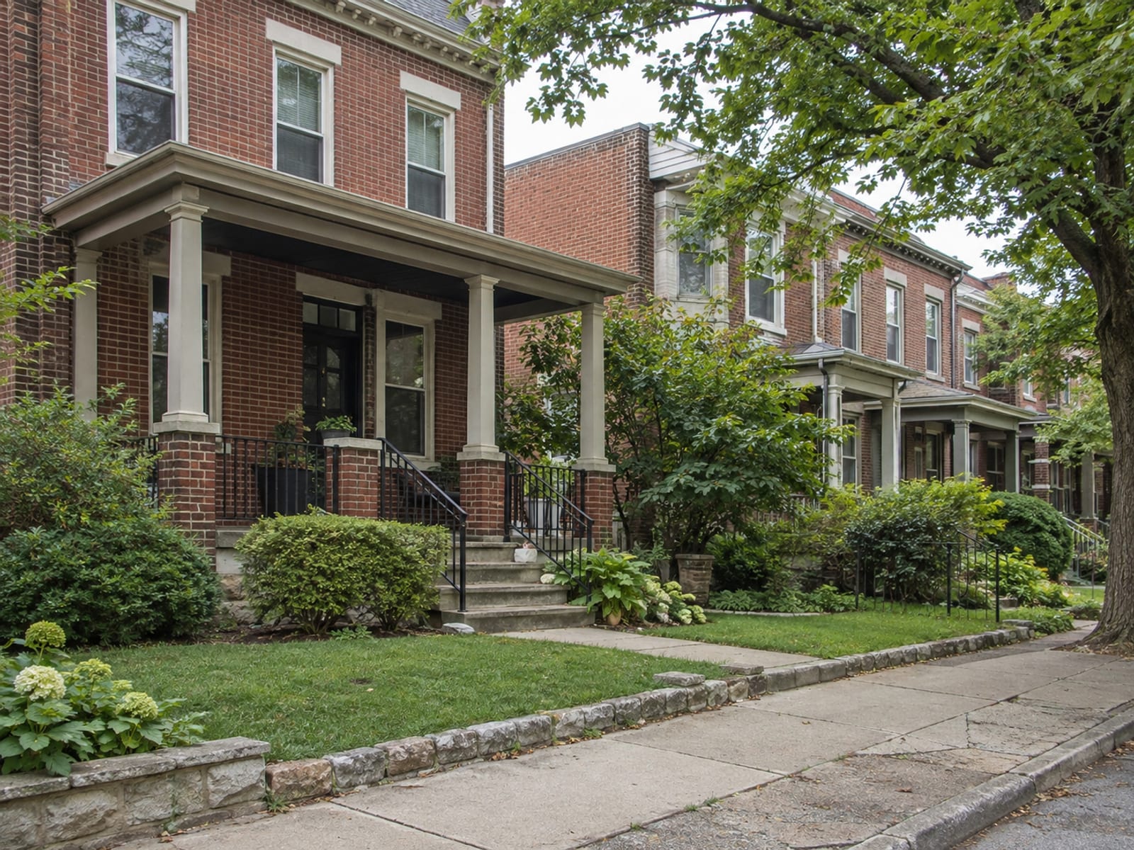 A brick row house with a small front yard on a quiet tree-lined street