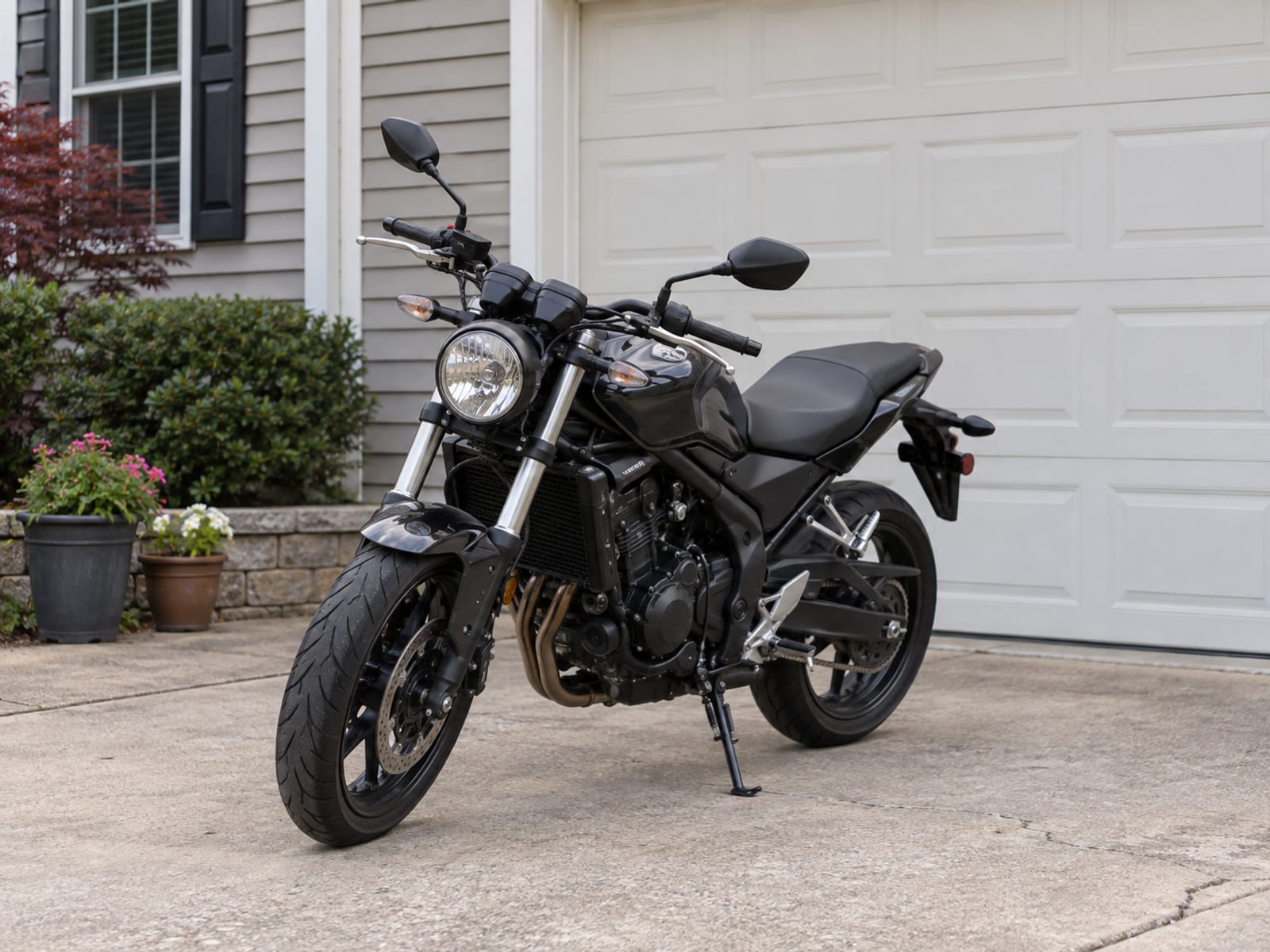 A motorcycle parked in a driveway beside a garage door on a sunny afternoon