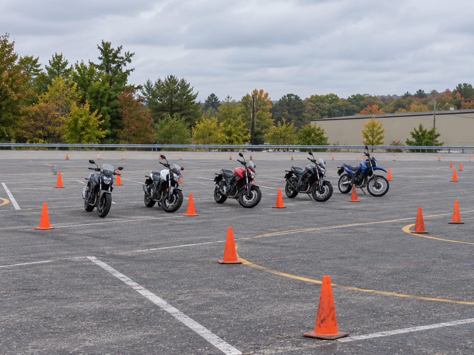 A row of small training motorcycles lined up beside traffic cones on an empty paved range