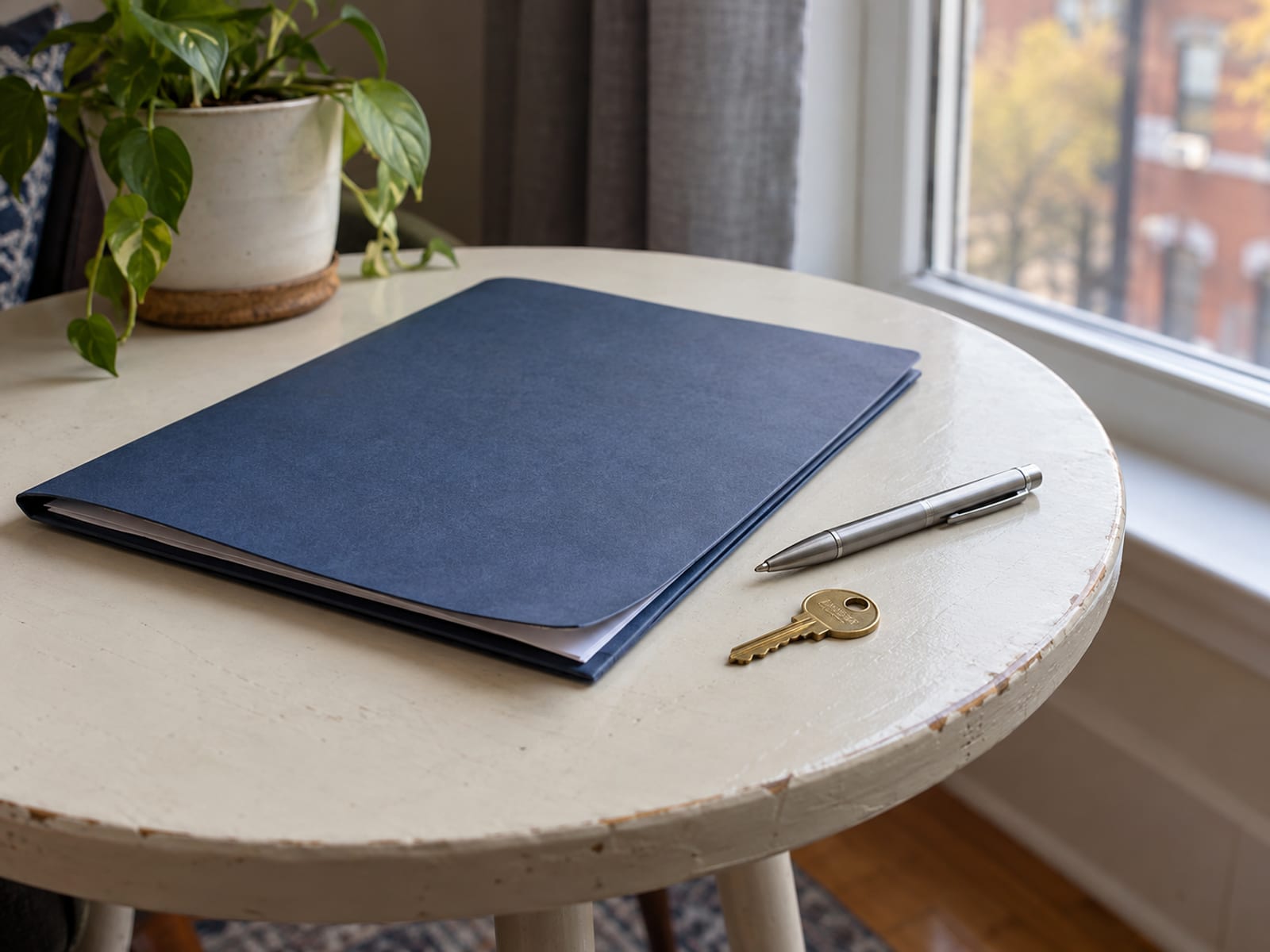 A lease folder, a pen and an apartment key on a small table by a window