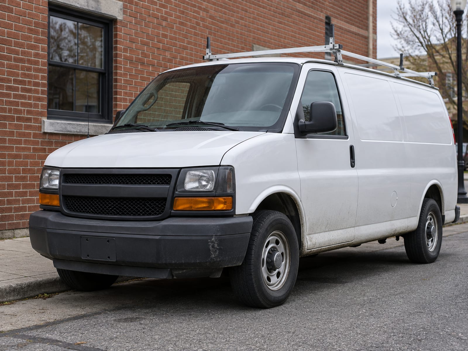 A plain white work van parked outside a brick commercial building on a Pennsylvania street