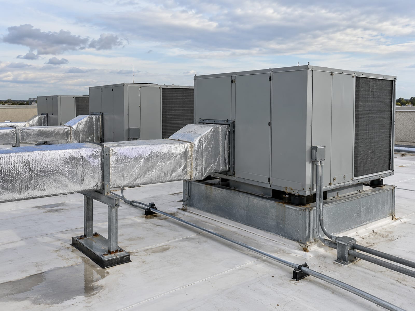 Rows of air handling units and insulated ductwork in a clean rooftop mechanical area of a commercial building